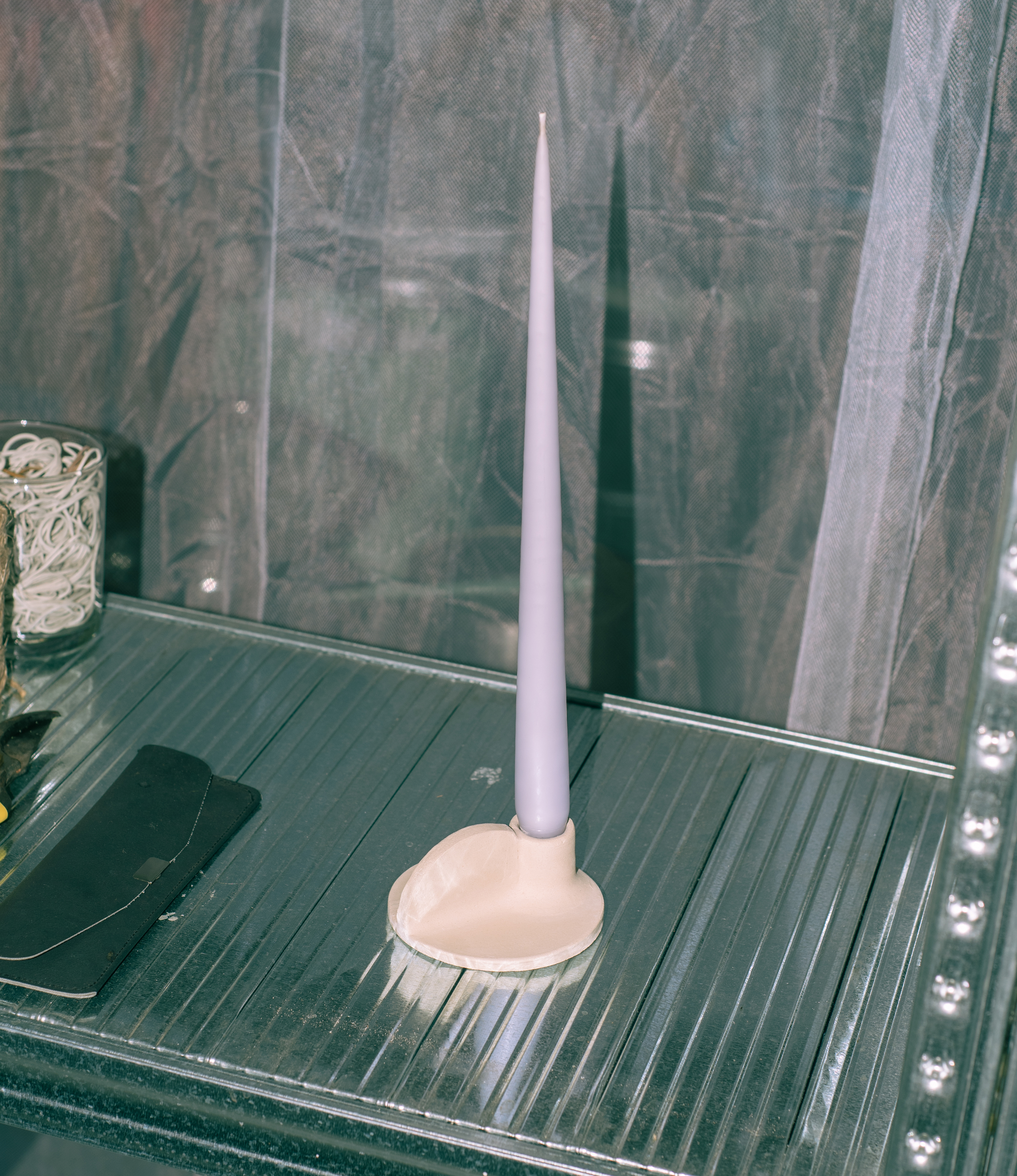 Myrtha Candle Holder is created by Alfareria La Nava. The product comes in a cream color and it has a natural matte finishing. In this picture the product is showcased on a steel shelf, with the lilac tapercandle from Ester and Eric