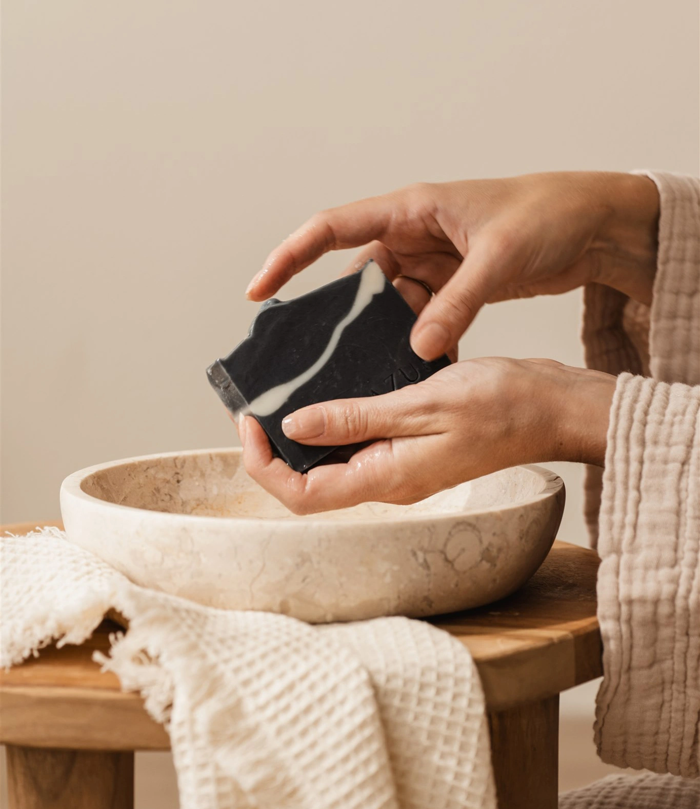Face Cleansing Soap in use by a hand. There is a bowl with water on the picture and a soft towl as well.