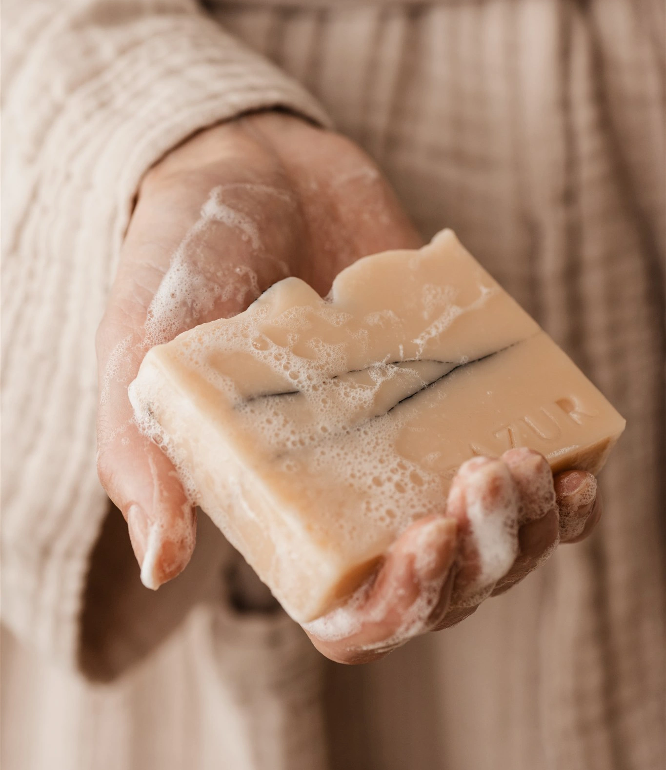 Wild Flower Soap from Azur in use. The item is held by a hand and it has a soft foam around it, as if the person was using it to wash her hands.