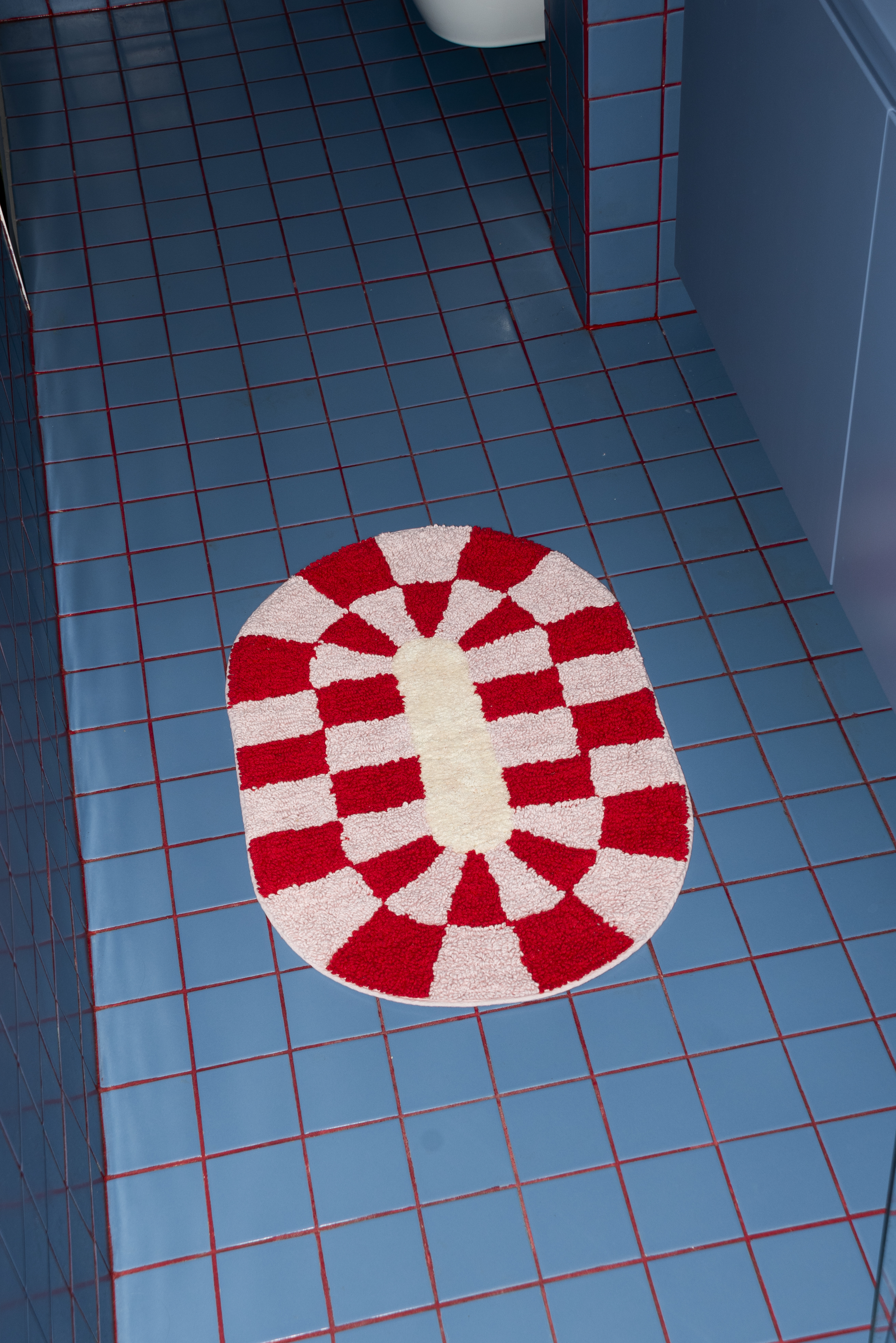 A closer look at Tarta Gelatina Miranda Bathmat in use, styled in a contemporary bathroom with blue tiles, showcasing its playful and functional design.