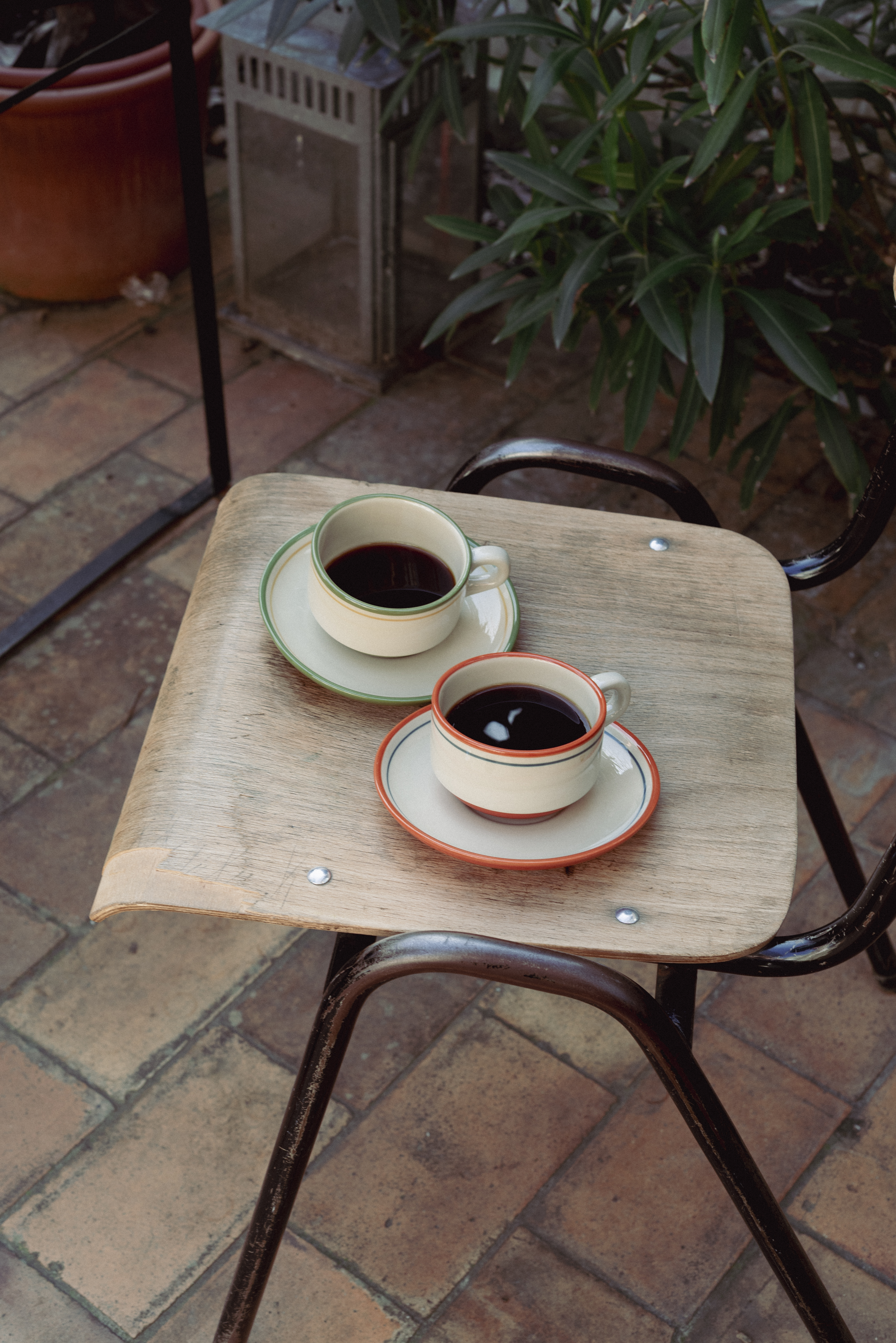 The two CAsa Atlantica Spanish Bar Cups laying on a chair in a garden and filled with coffee