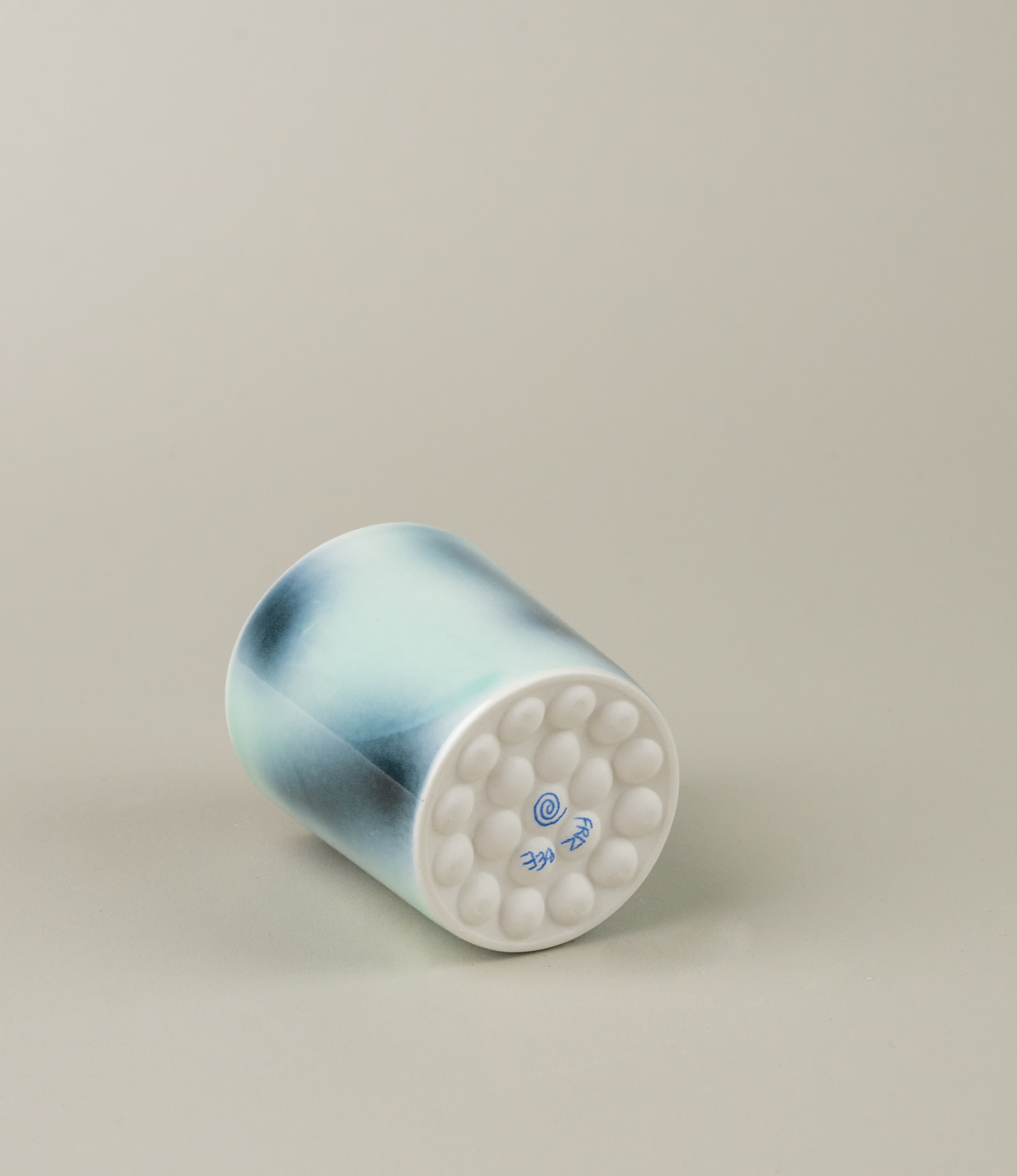 Bulle Cup from Frizbee Ceramics has a unique gradient painted pattern. The product has cold colors like green, dark and light blue. The bottom of the cup looks like it's made of small bubbles. On this picture a hand is holding the cup.