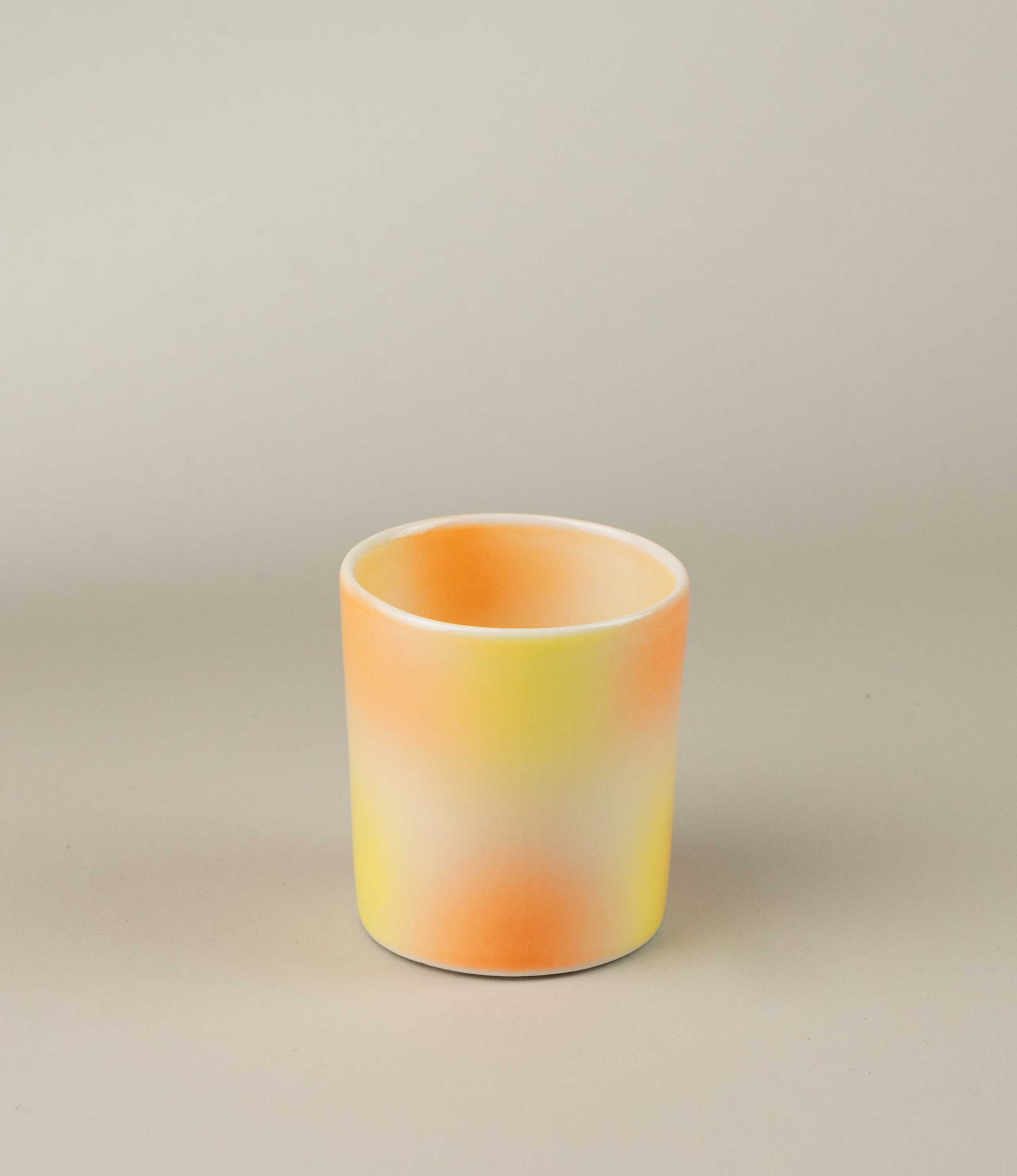Bulle Cup from Frizbee Ceramics has a unique gradient painted pattern. The product has warm colors like orange, peach and yellow. The bottom of the cup looks like it's made of small bubbles.