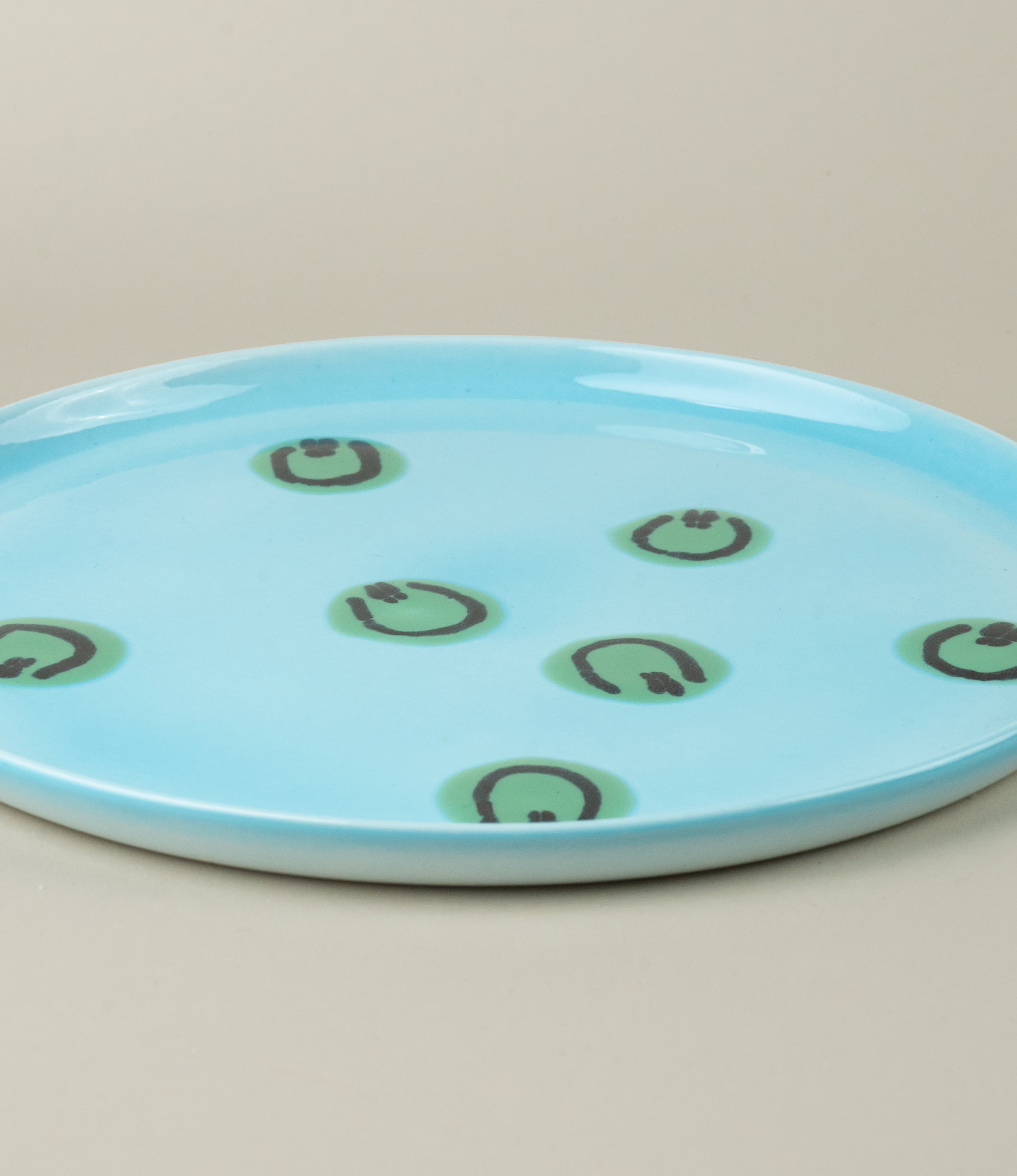 A closeup of Frizbee Ceramics' Blue Alien Plate. The green smiley pattern is placed on a light blue base.