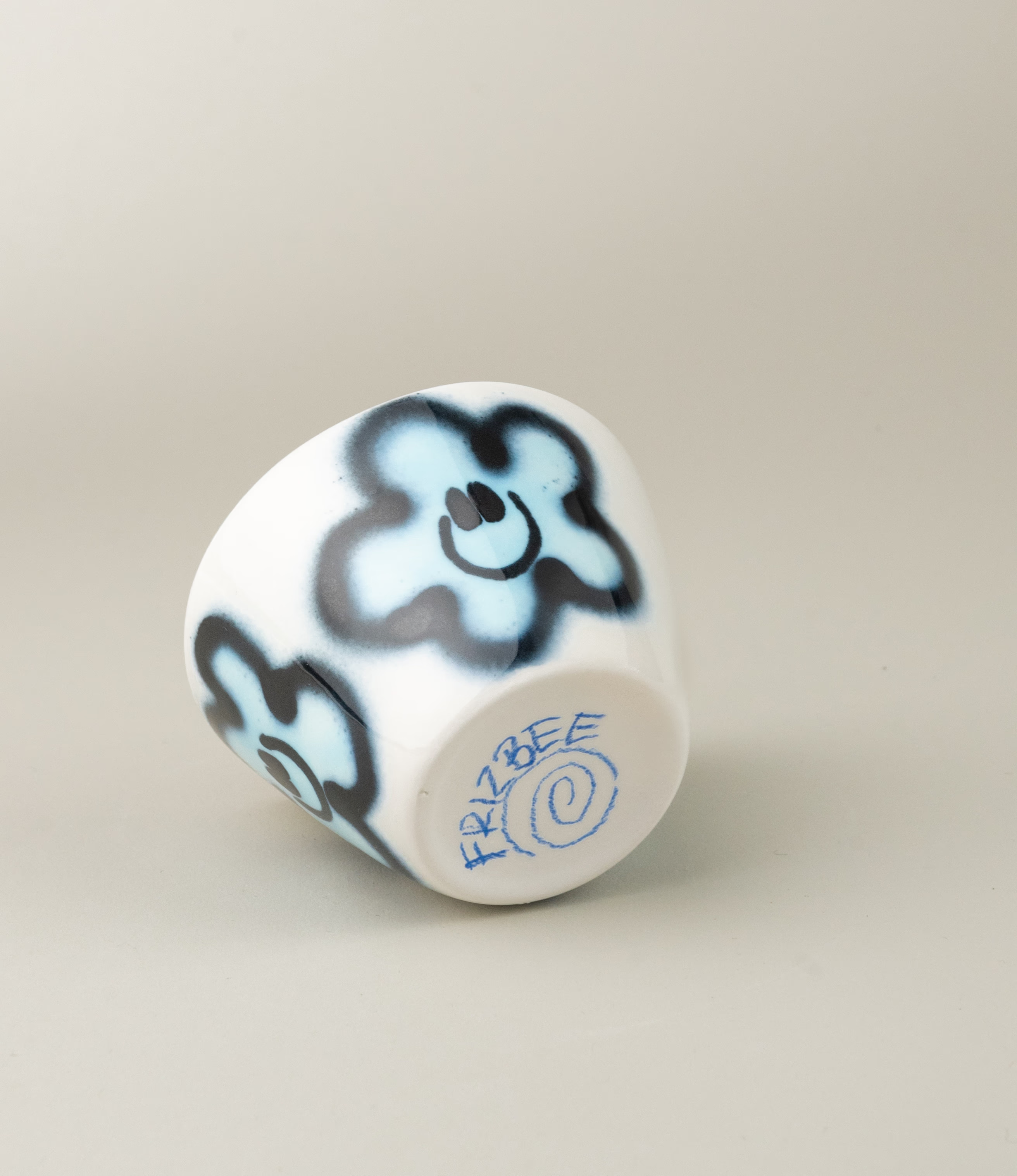 Super Cup from Frizbee Ceramics. The cup's base is white with a blue flower smiley. In this picture a hand is holding the cup.
