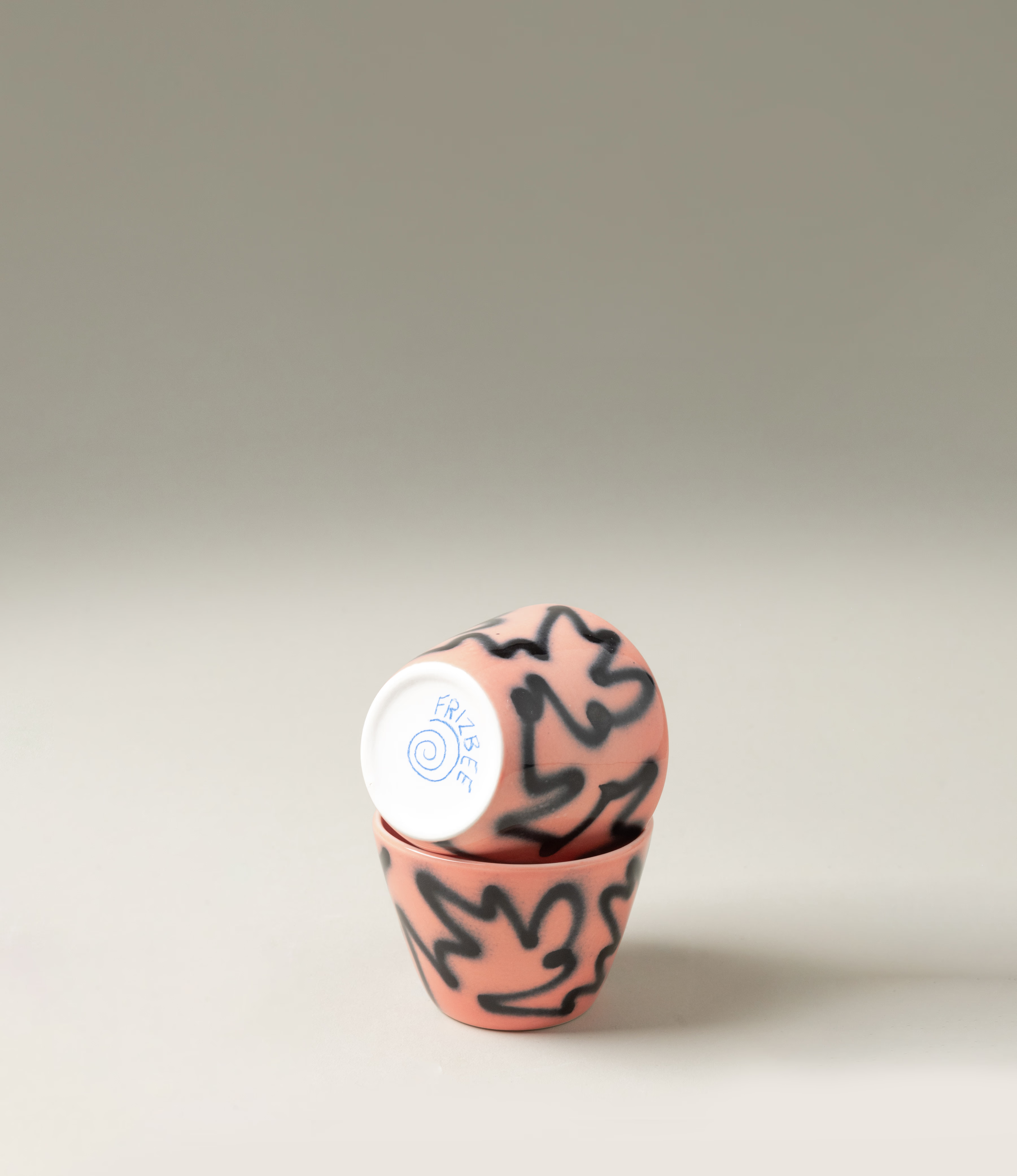 Super Cup from Frizbee Ceramics is a set of two cups. The cups' base is peach with a black graffiti like zig-zag painting on it.