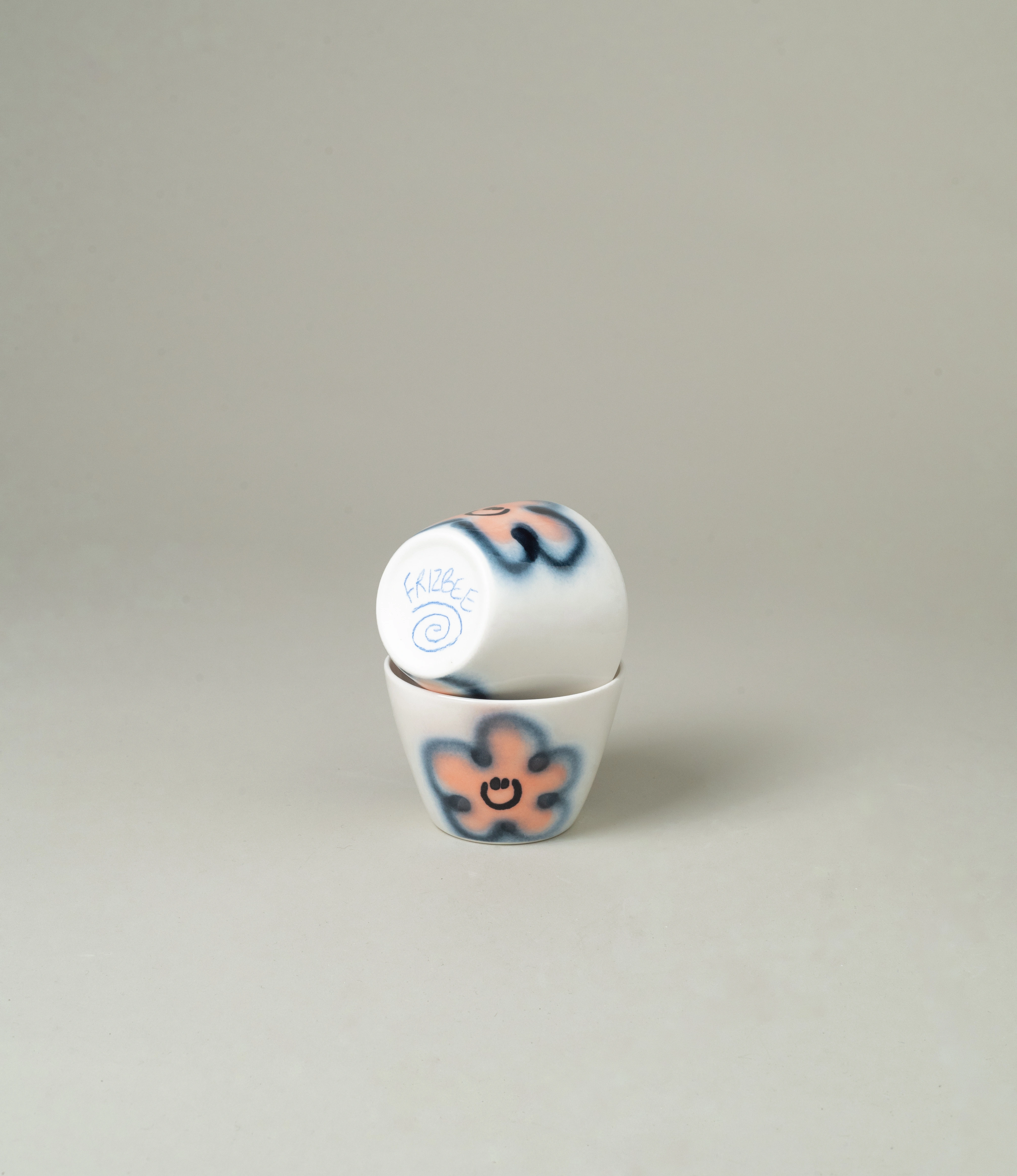 Frizbee Ceramics Super Cup in Peach Carne, featuring playful hand-painted smiley flowers in pink and blue tones. A whimsical and unique addition to your drinkware collection.