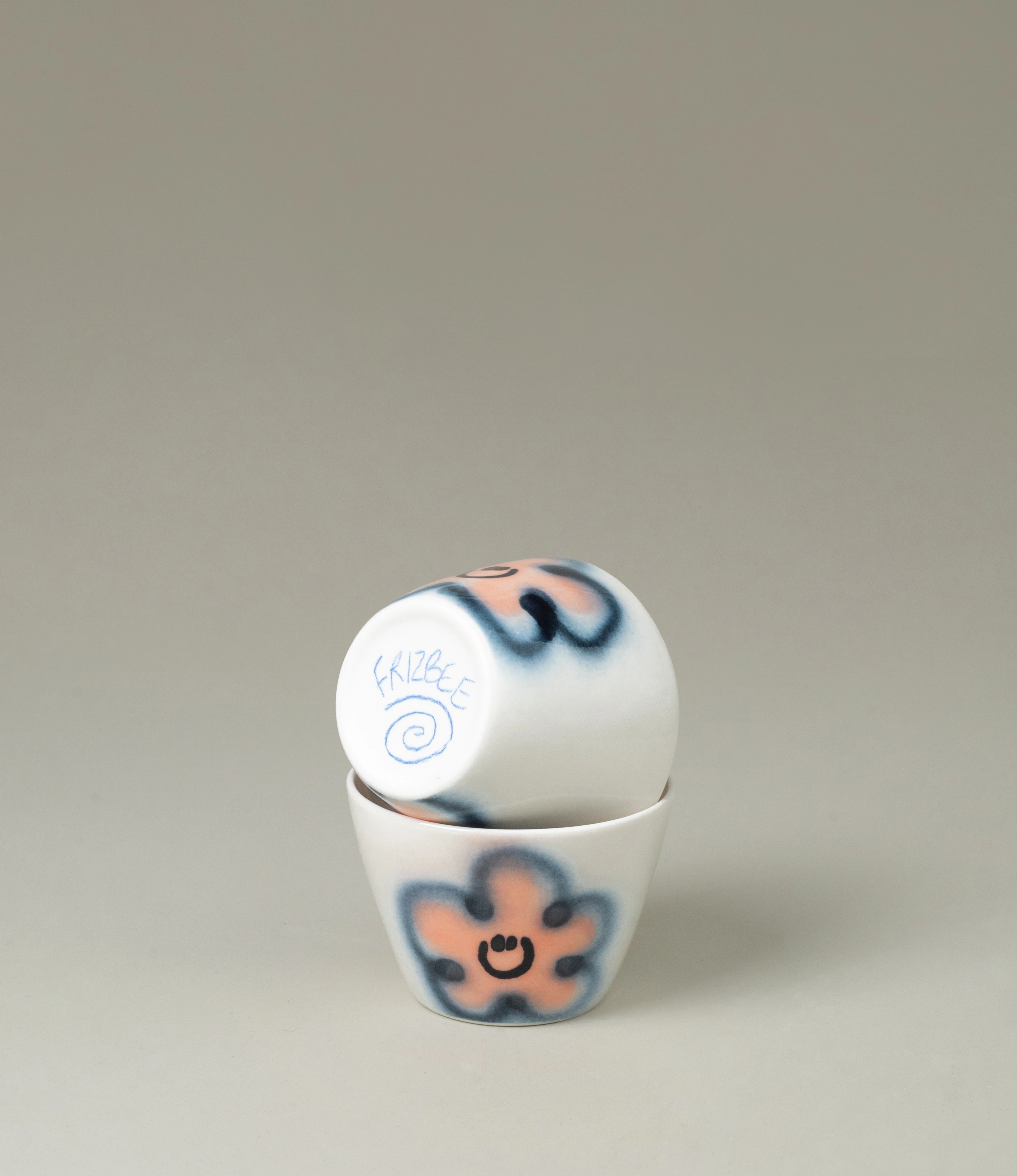 Frizbee Ceramics Super Cup in Peach Carne, featuring playful hand-painted smiley flowers in pink and blue tones. A whimsical and unique addition to your drinkware collection.