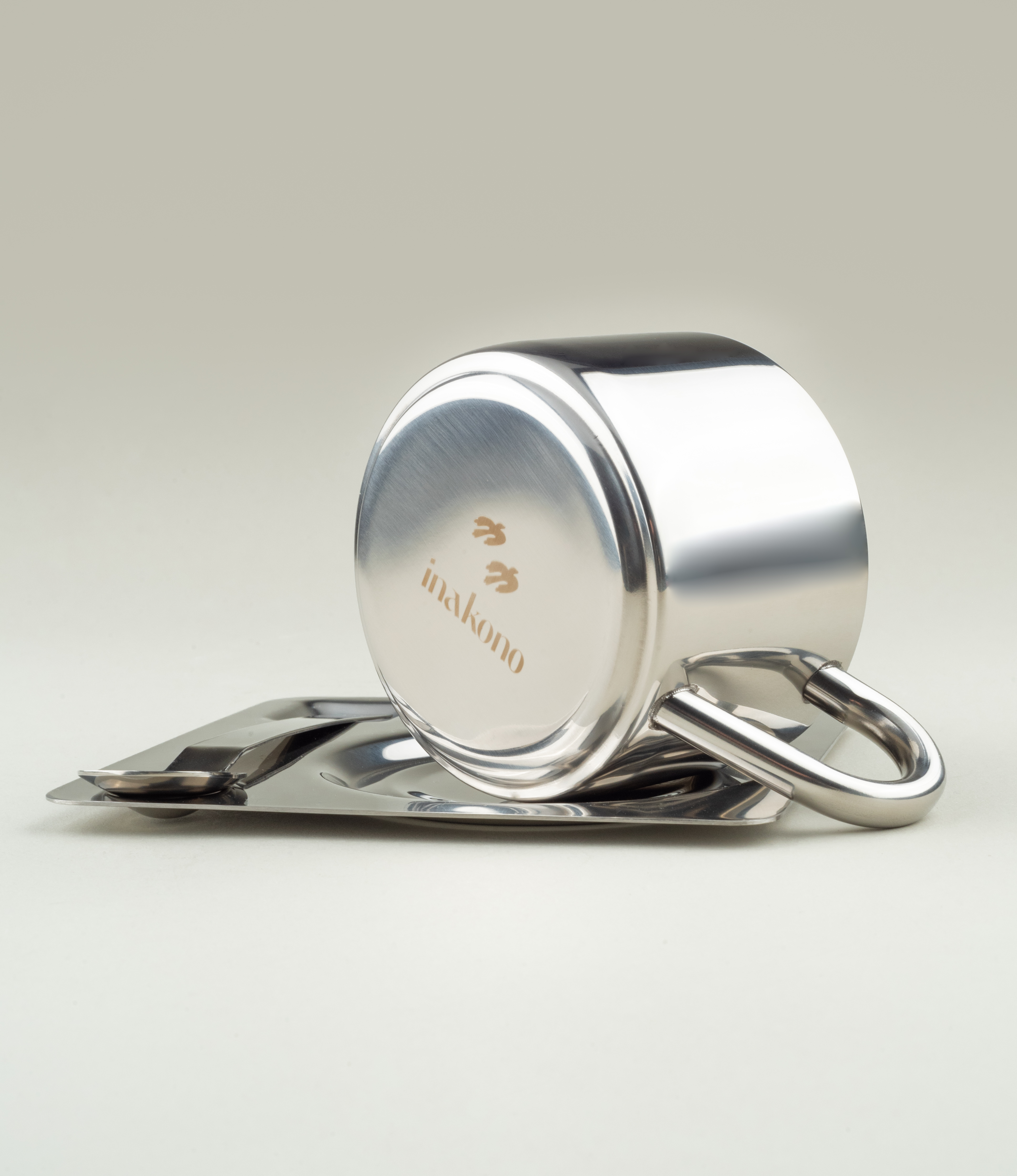 Low side angle of the stainless steel set with the cup tipped to reveal the Inakono logo engraved on its base