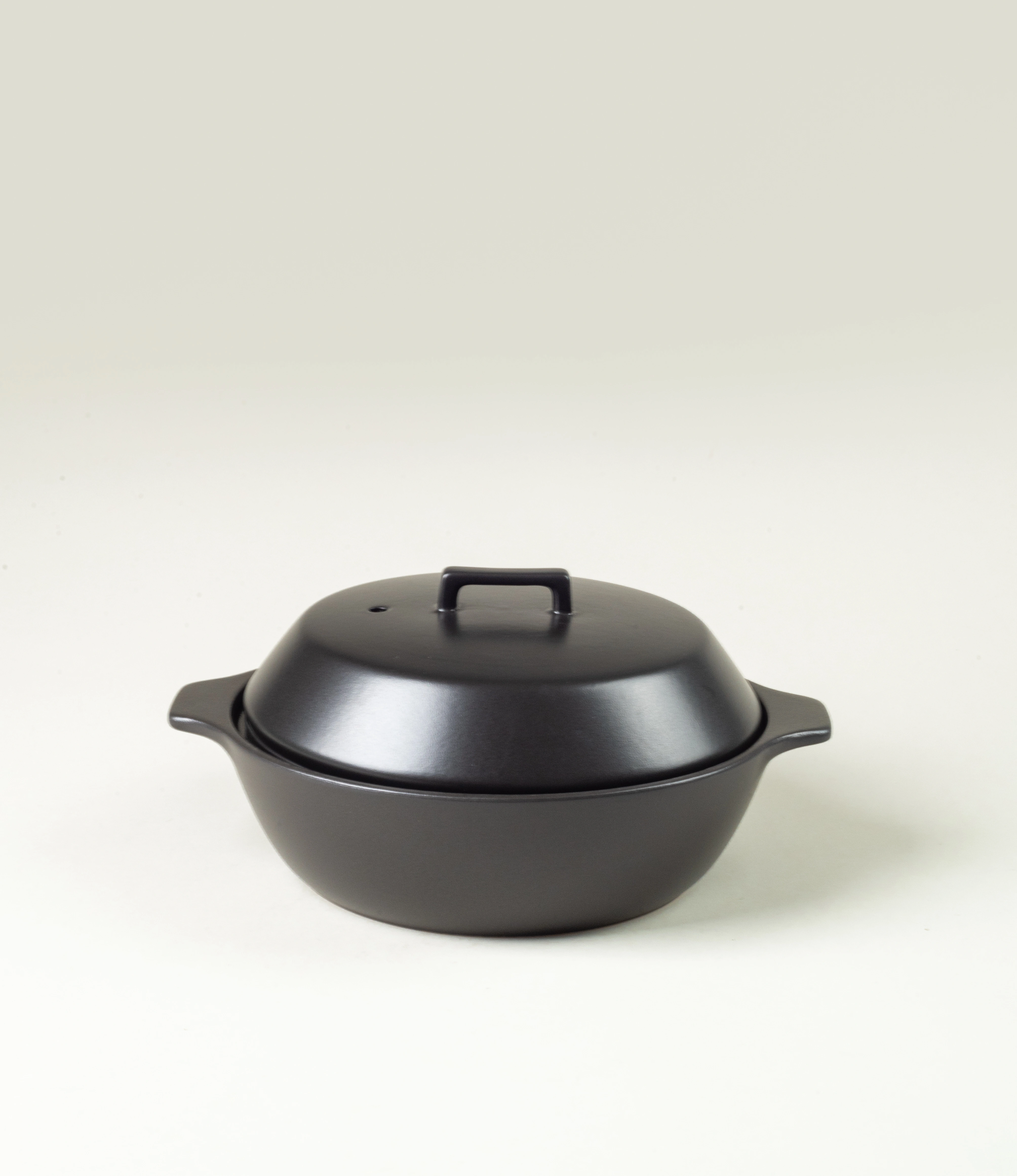 Kinto Kakomi Black Ceramic Pot with a minimalist design, featuring a rounded lid and sturdy handles. Perfect for slow cooking and presenting meals with understated elegance.