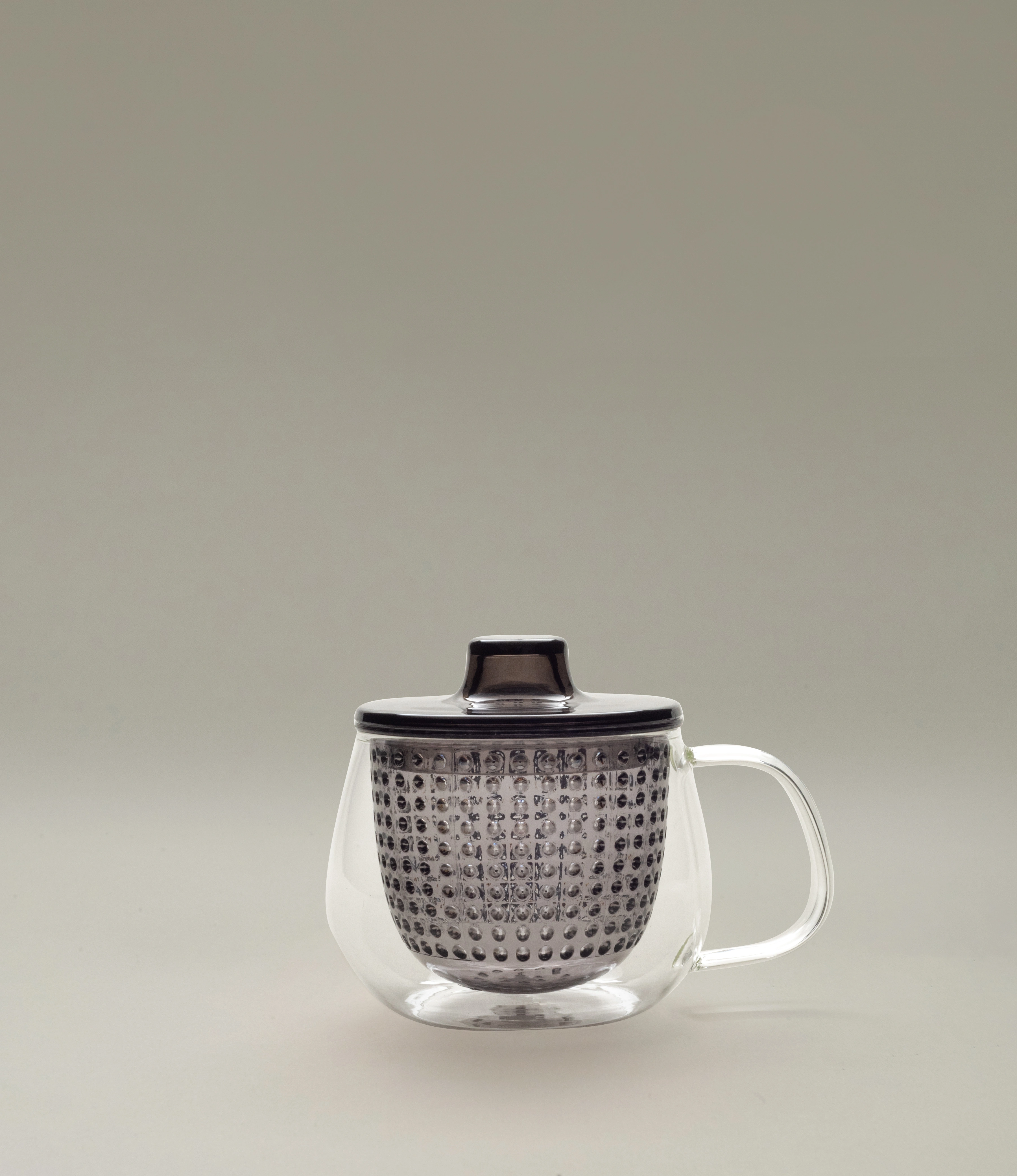 Kinto Unimug in dark smoky grey, showcasing a double-walled glass mug with a perforated tea infuser and matching lid, displayed on a neutral grey background.