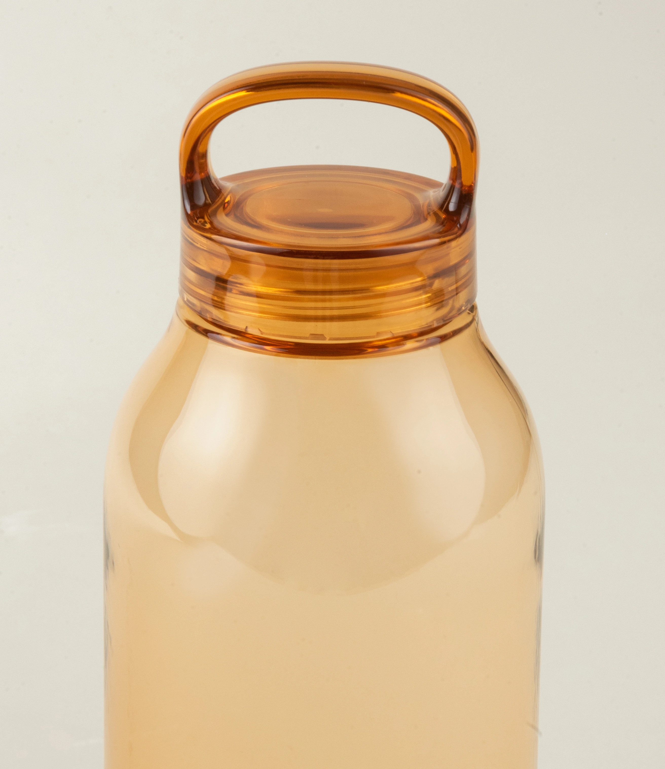 Close-up view of the amber-colored water bottle's top, highlighting the ergonomic integrated handle and the smooth, translucent plastic material. The design emphasizes functionality and a modern aesthetic.