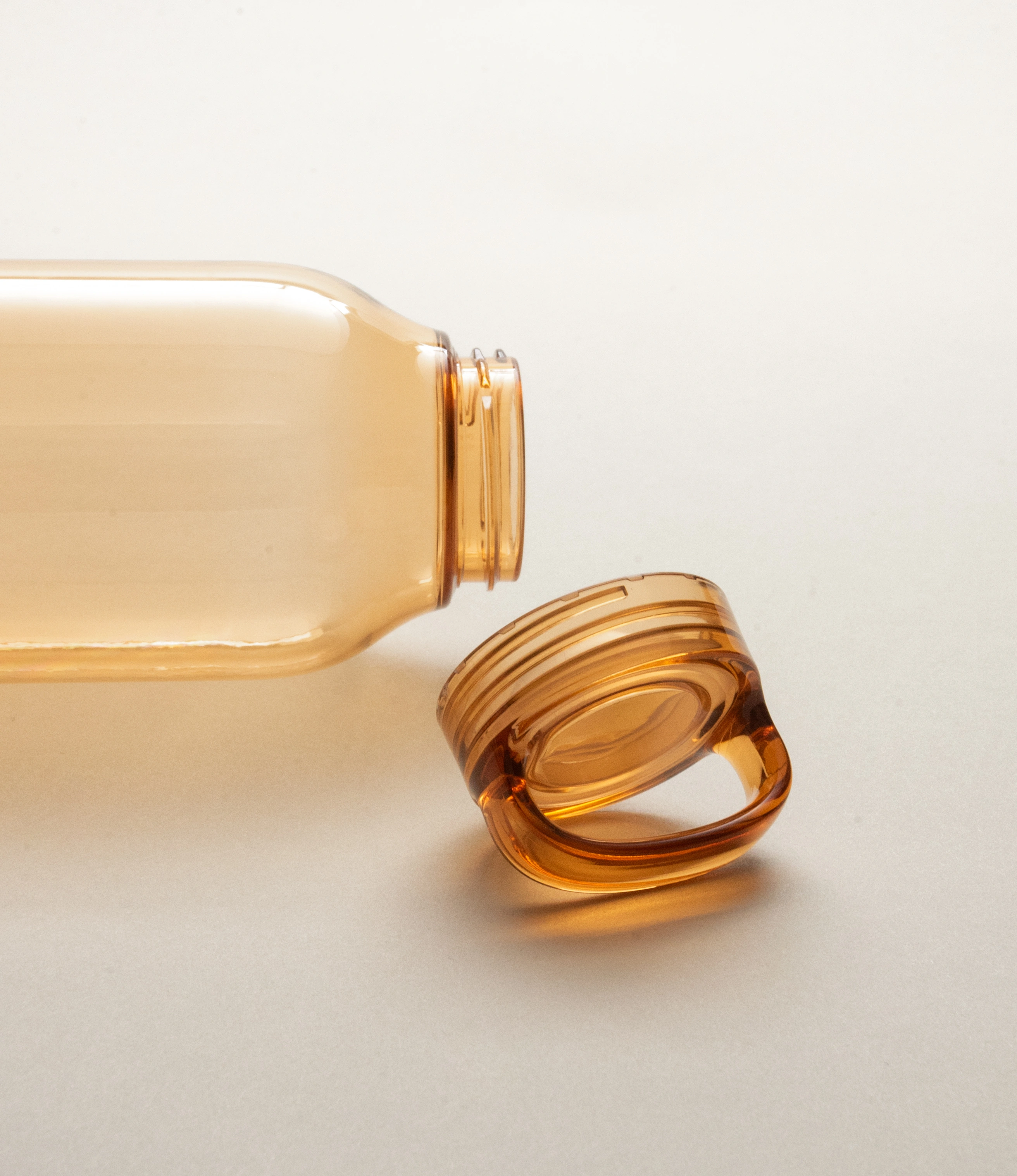 Close-up of an amber-colored Kinto water bottle lying on its side with the cap detached and placed beside it. The smooth and minimalist design of the bottle and cap is highlighted against a neutral background.