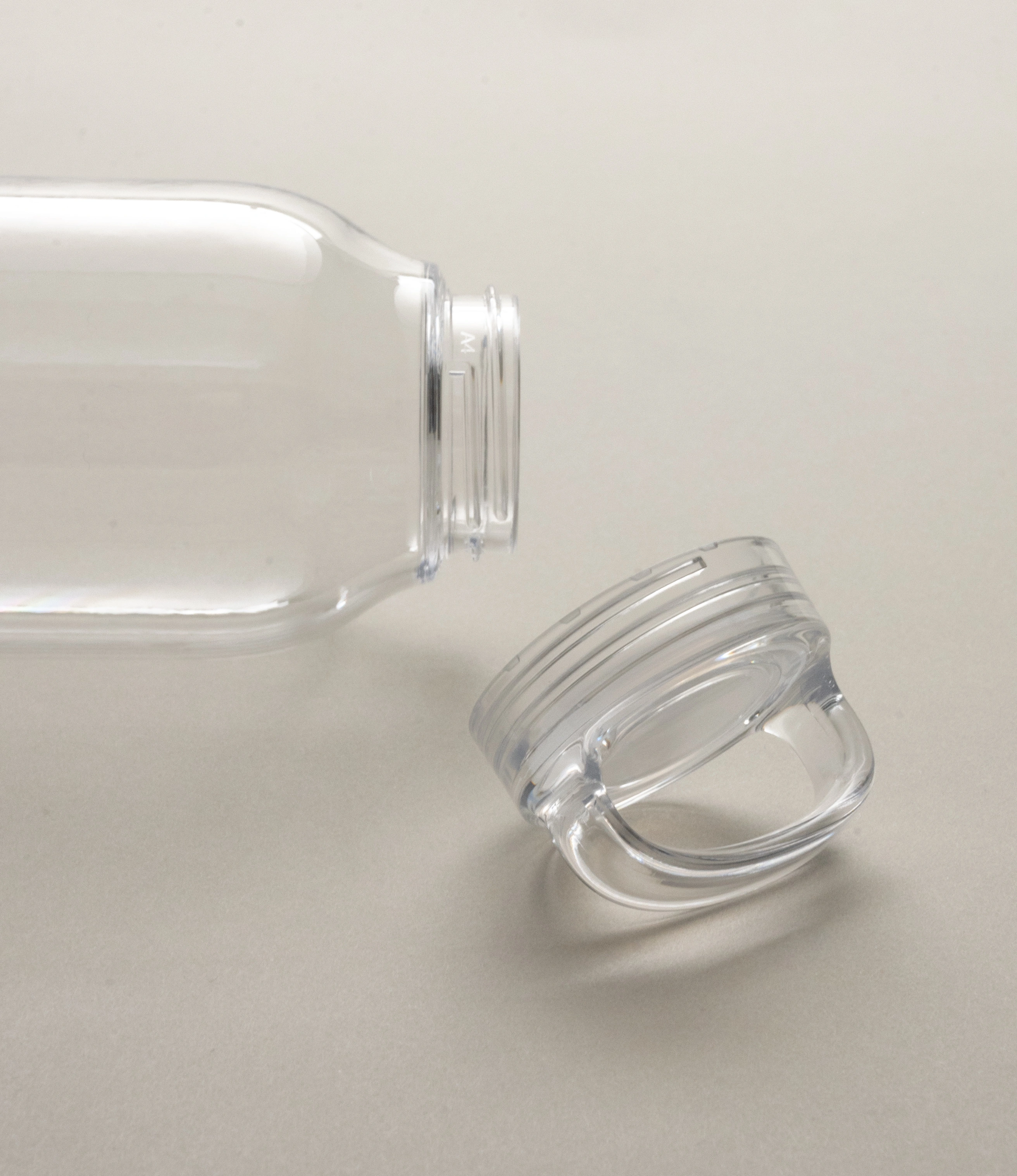 Close-up of a clear Kinto water bottle lying on its side with the cap detached. The bottle’s transparent material highlights its clean and simple design, while the looped cap rests nearby on a neutral background.