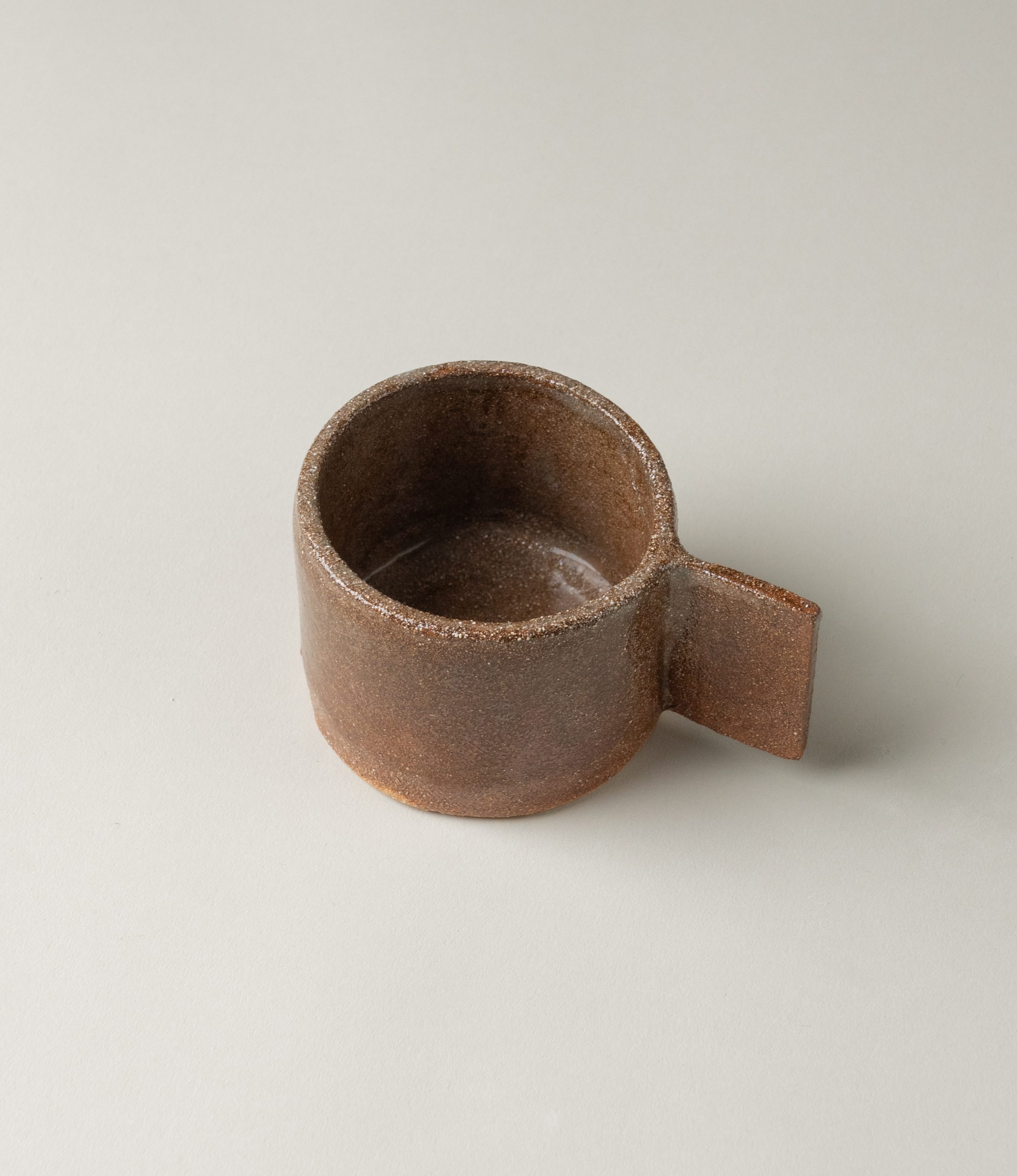 Ceramic cup from Manamo Cup. The item comes in the soothing earthy coffee color. The handle has an unusual rectangle shape which makes the modern touch to the natural tone and texture. This pictures shows the product from the top.