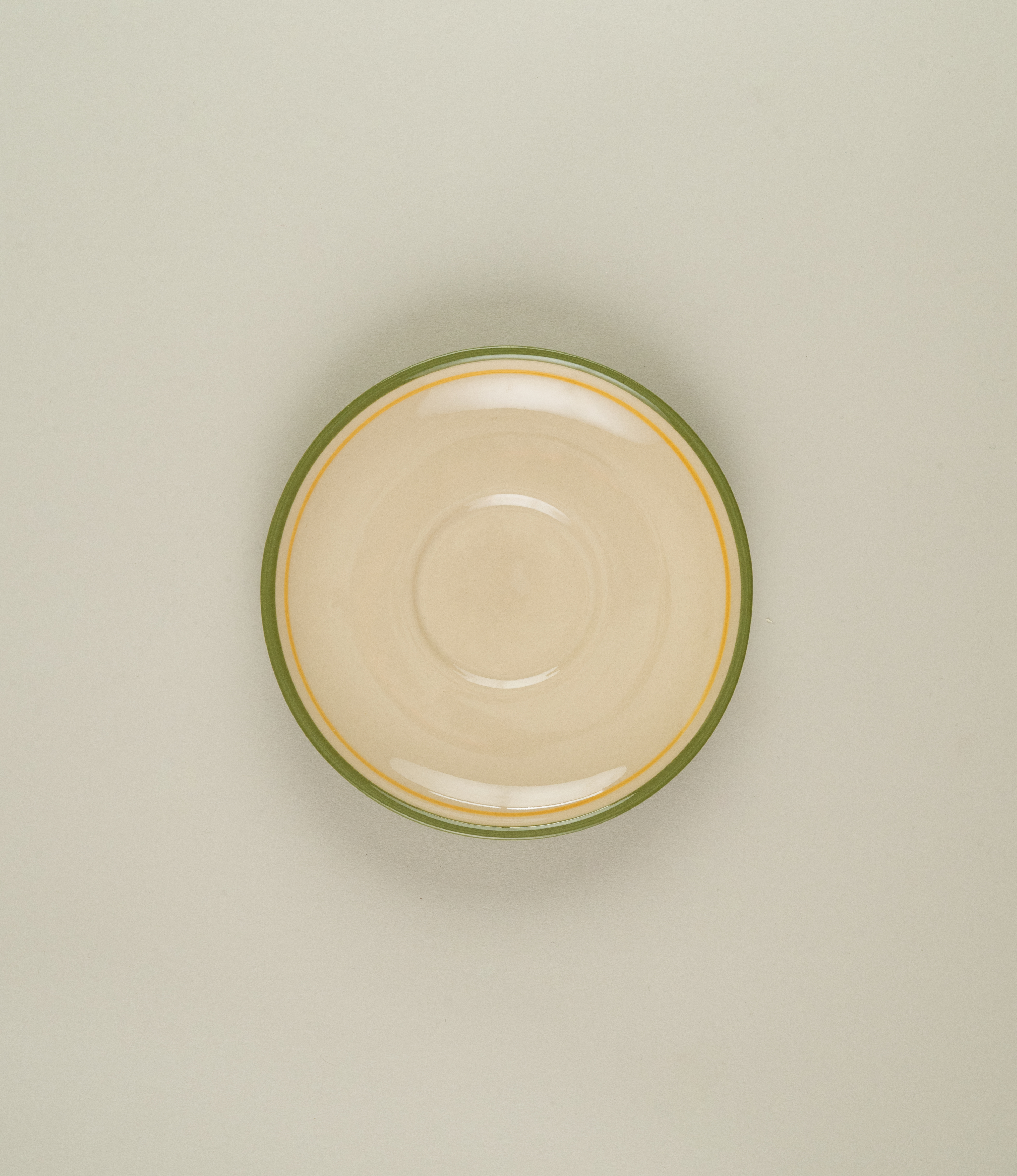 Top view of Casa Atlântica green stoneware coffee saucer, featuring hand-painted green and yellow rings on a natural clay base.