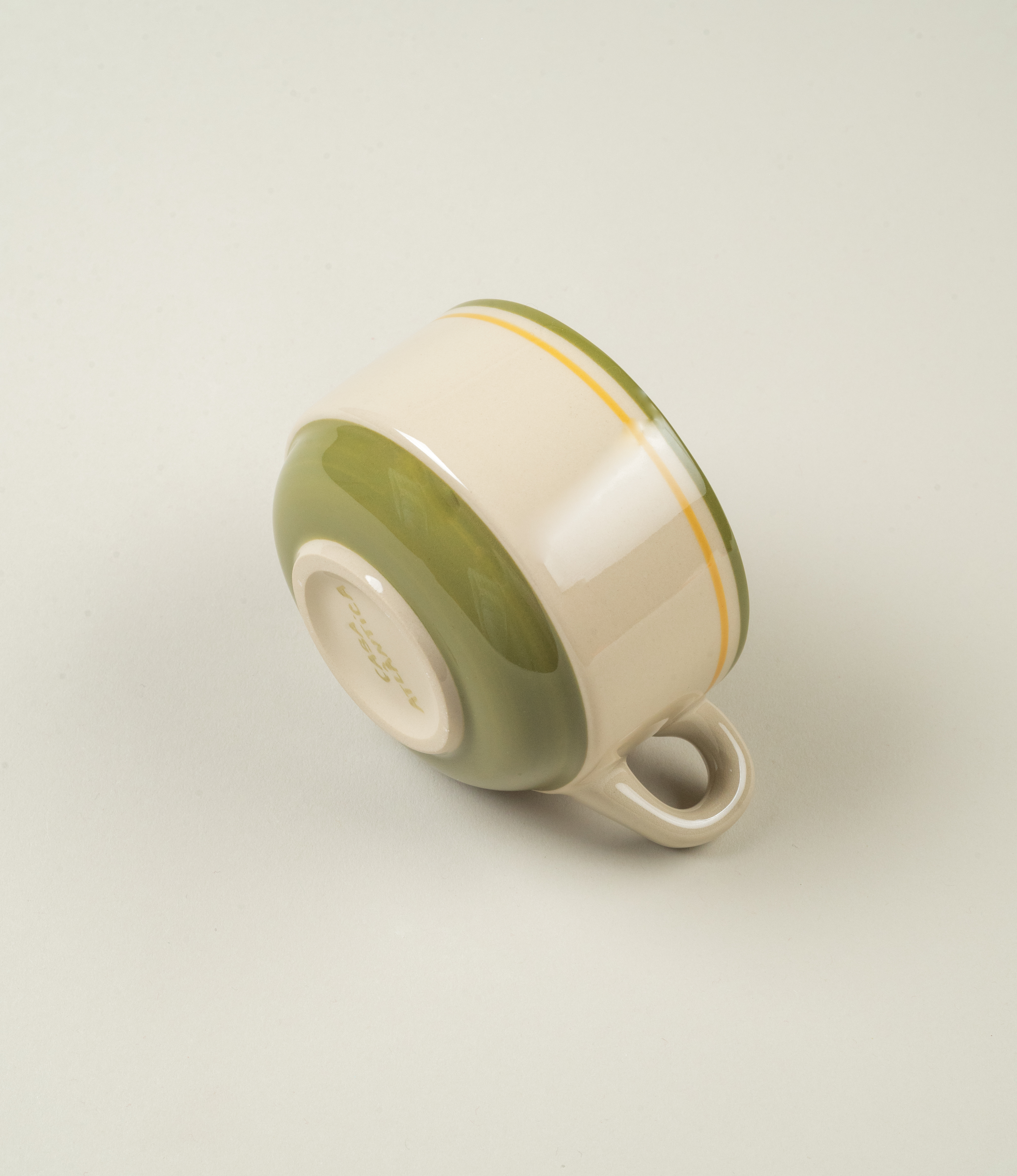 Side angle of Casa Atlântica green coffee cup lying on its side, displaying glazed green base and hand-painted rim detailing.