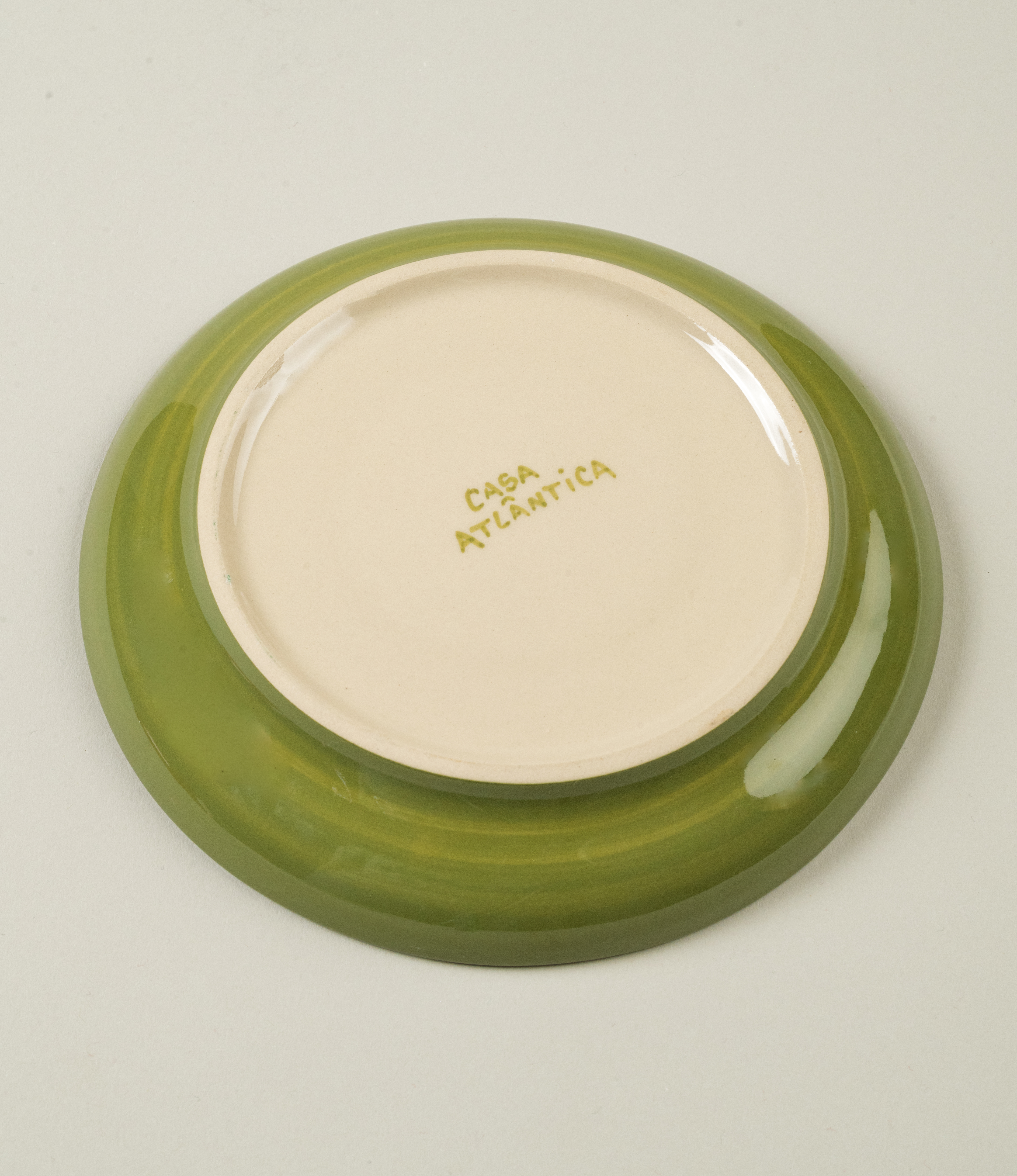 Underside of Casa Atlântica green saucer showing glossy glaze and brand name hand-painted on the unglazed base.