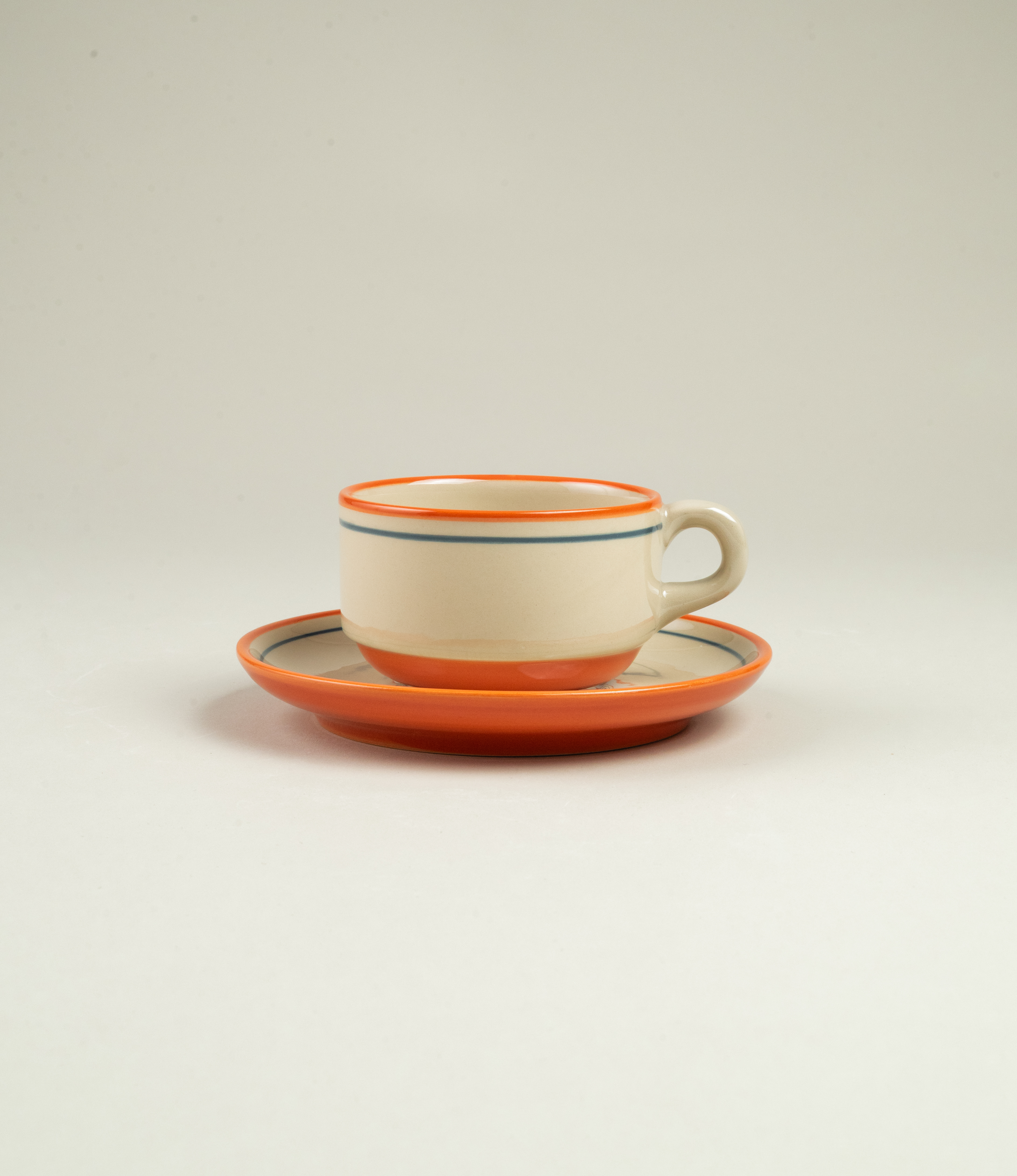 Side view of Casa Atlântica coffee cup and saucer in stoneware, featuring hand-painted detailing in orange and blue tones.