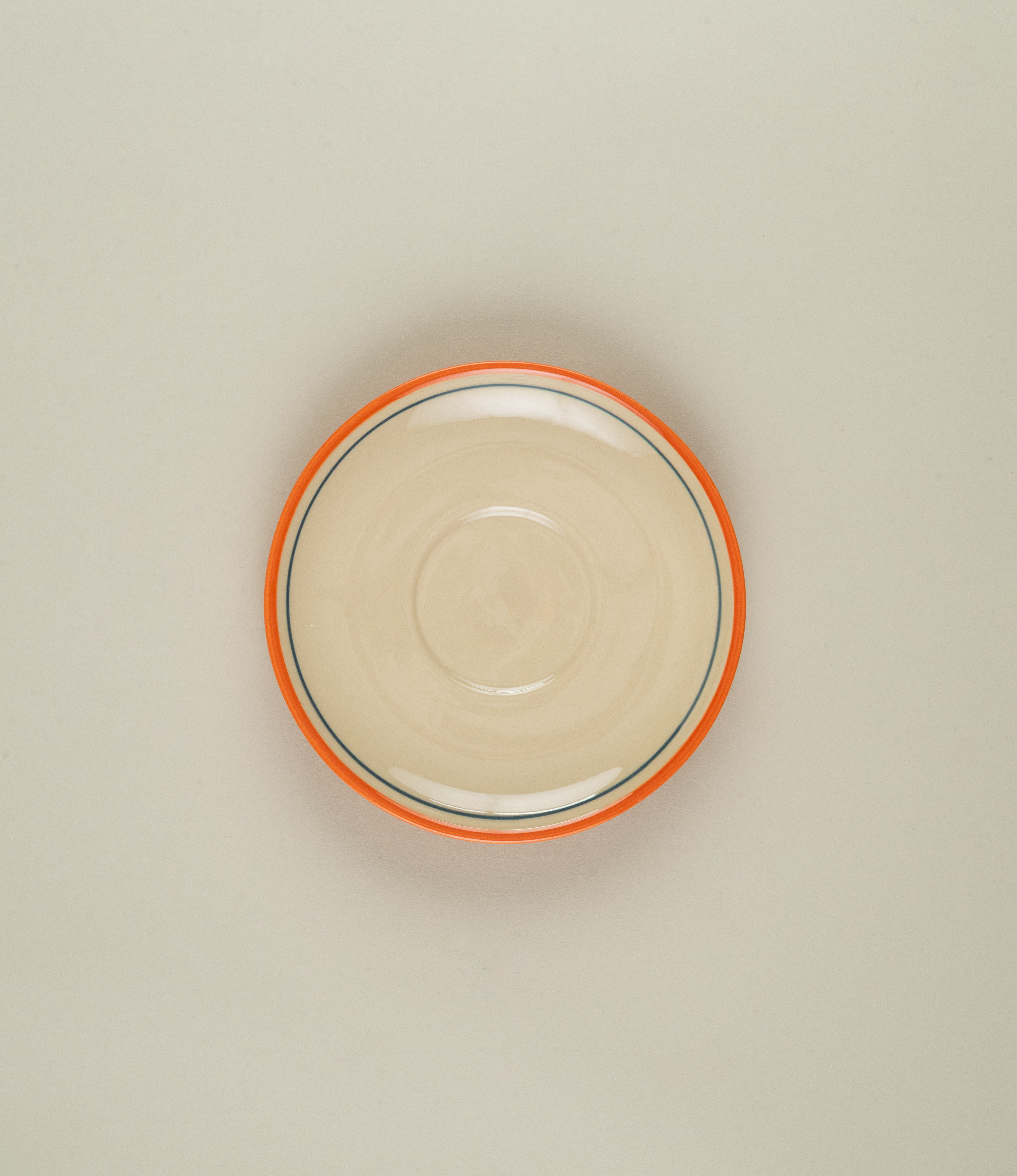 Overhead shot of Casa Atlântica stoneware coffee saucer with hand-painted orange rim and fine blue line detailing.
