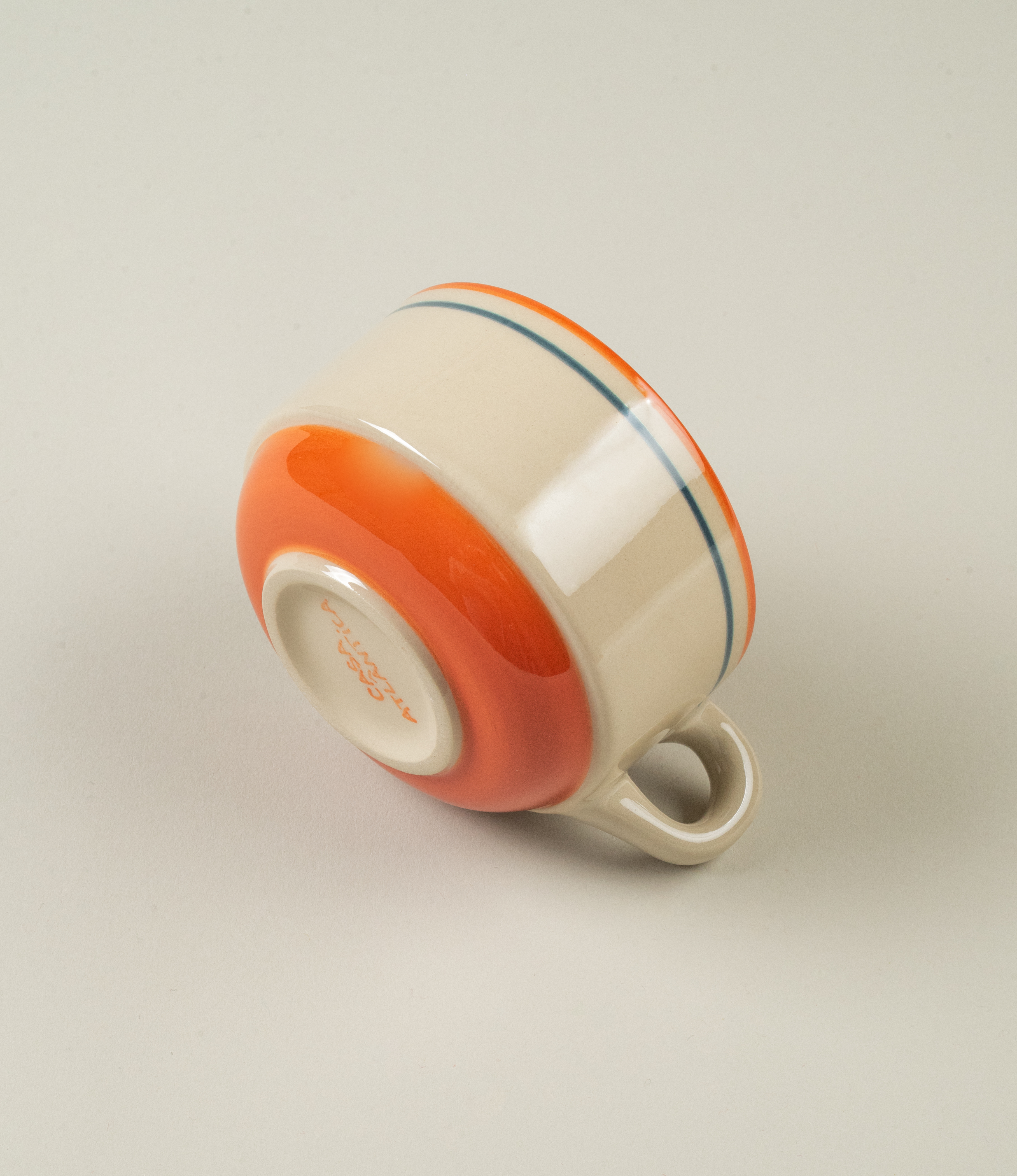 The coffee cup shown upside down, highlighting the orange glazed base and the brand name “Casa Atlântica” hand-painted underneath.