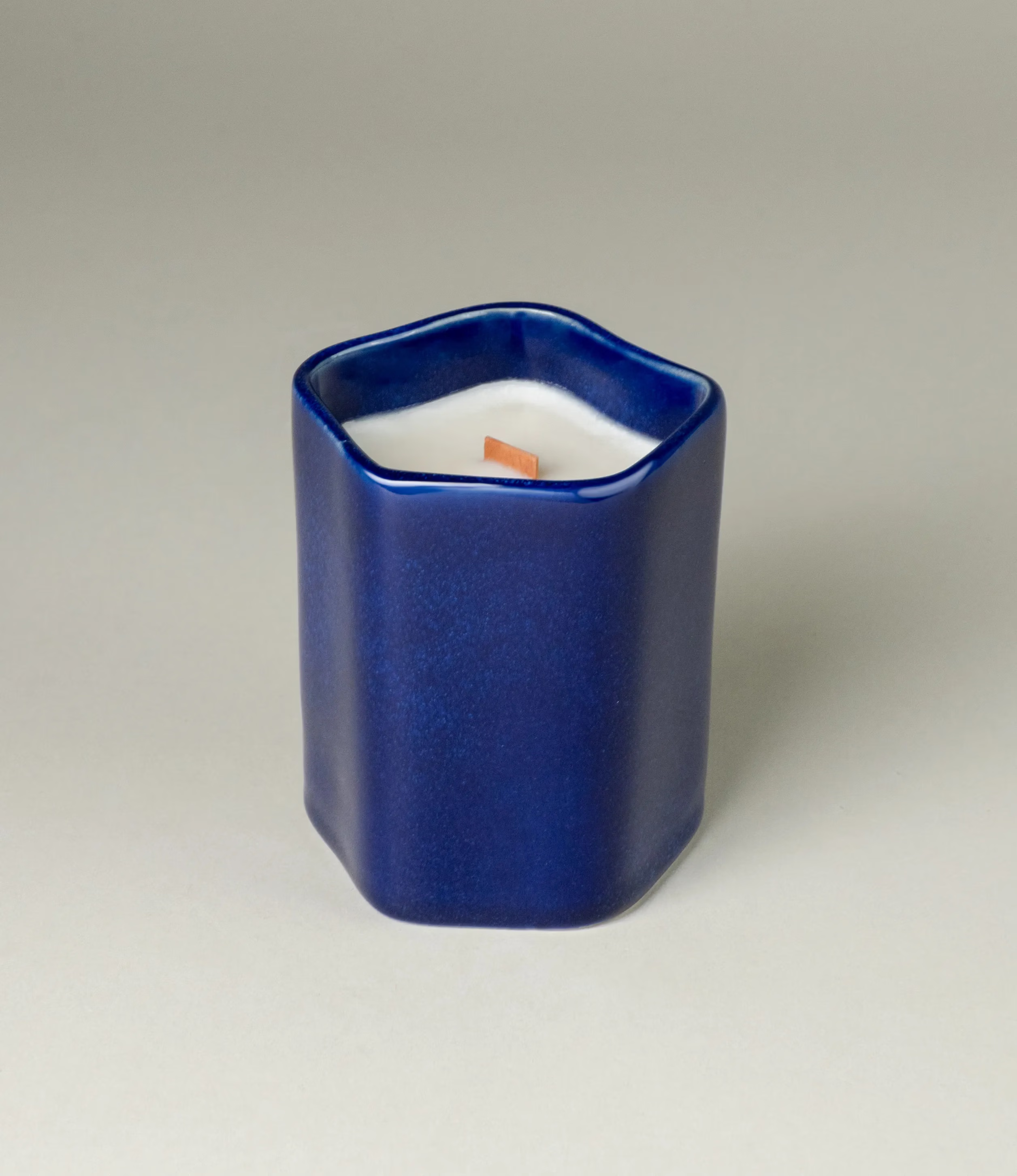 A scented Wax Candle designed by Ocactuu. The candle has an amber scent and it comes in a glossy dark blue ceramic. The material has a subtle spotted texture. The candle wick is made of wood for a more natural feeling.  