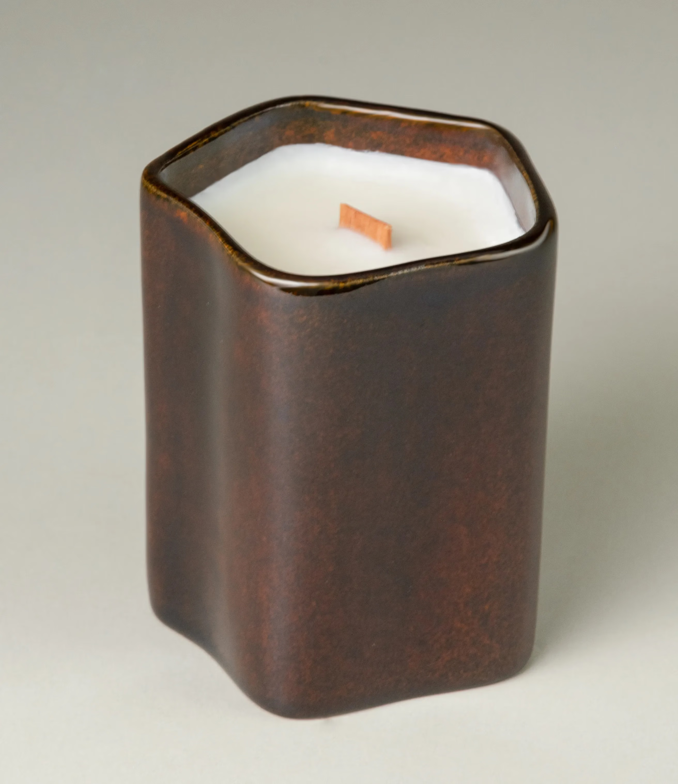 A scented Wax Candle designed by Ocactuu. The candle has a peach scent and it comes in a glossy dark brown ceramic. The material has a subtle spotted texture. The candle wick is made of wood for a more natural feeling.  
