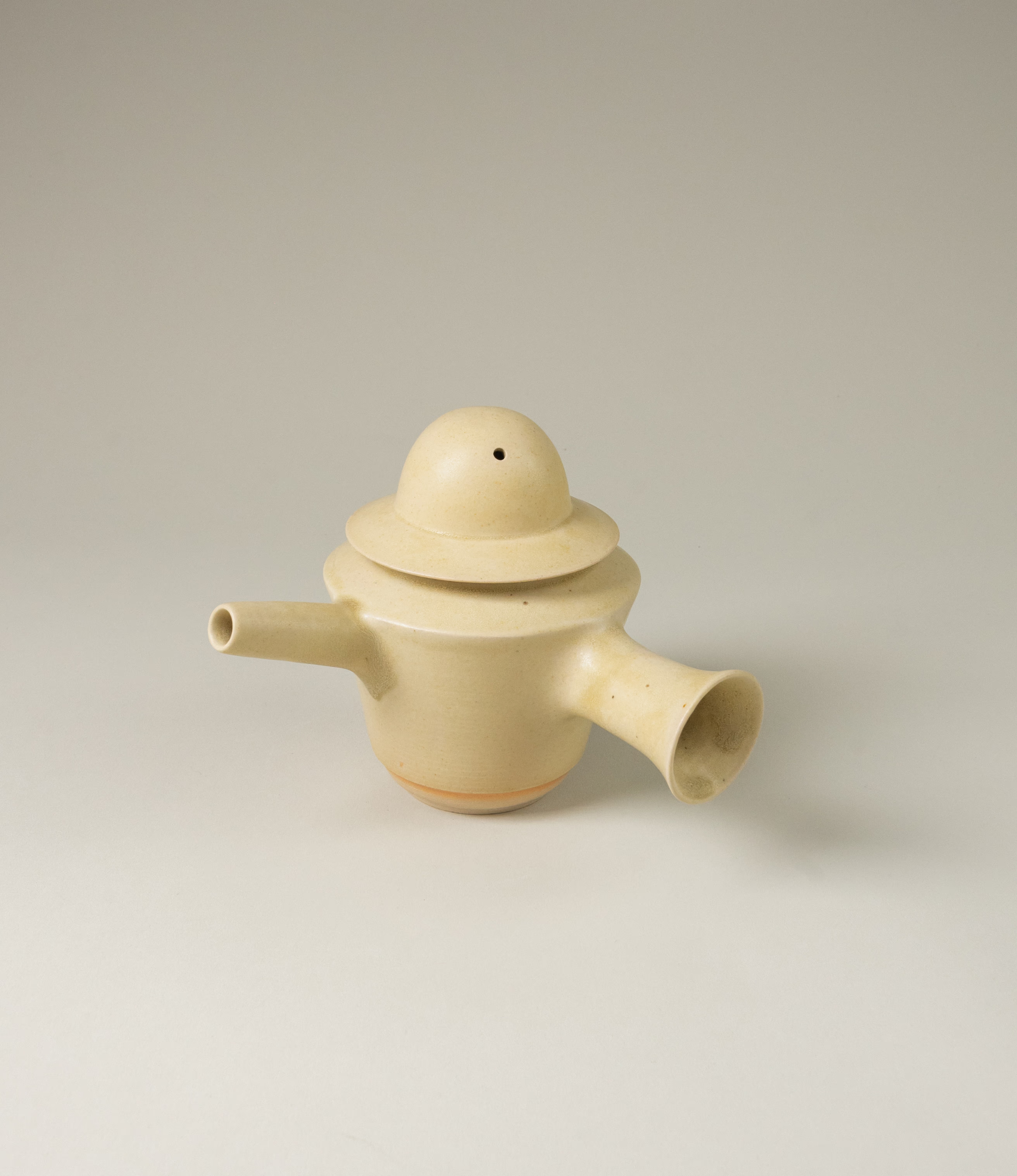 A special teapot from Omni Ceramics. The product adds a spice to the Omni tea collection. The lid of the teapot resembles a hat. The item comes in a light beige color, and with the unique painted orange gradient ring on the lower part of the product.