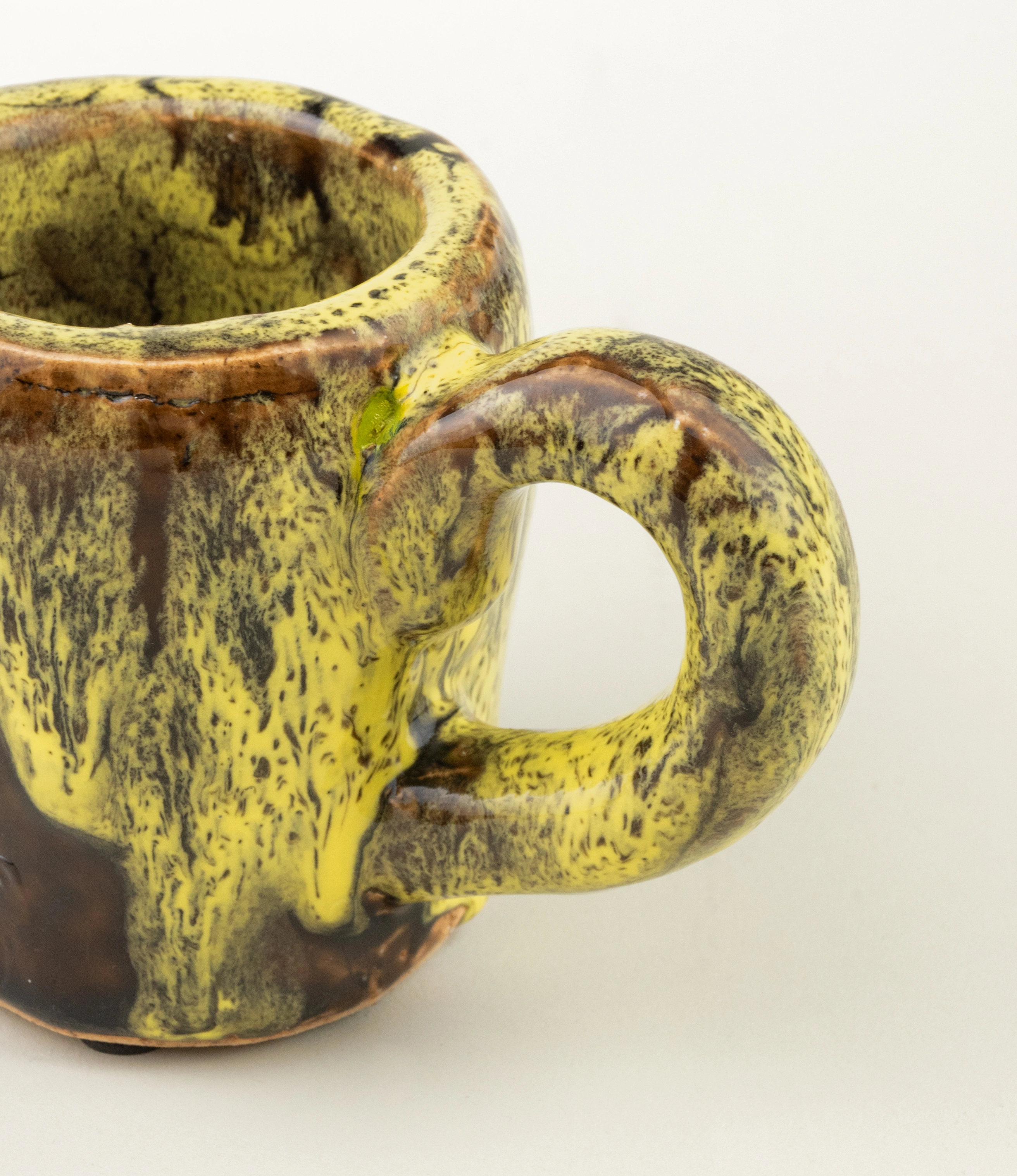 Cafeflamengo decorative cup from Serax. The cup is not suitable for drinking from it but can be perfect to store items on your desk. The cup has a special glazing with a dripping effect on it. The base of the cup is brown and the dripping is yellow. The item is handmade.