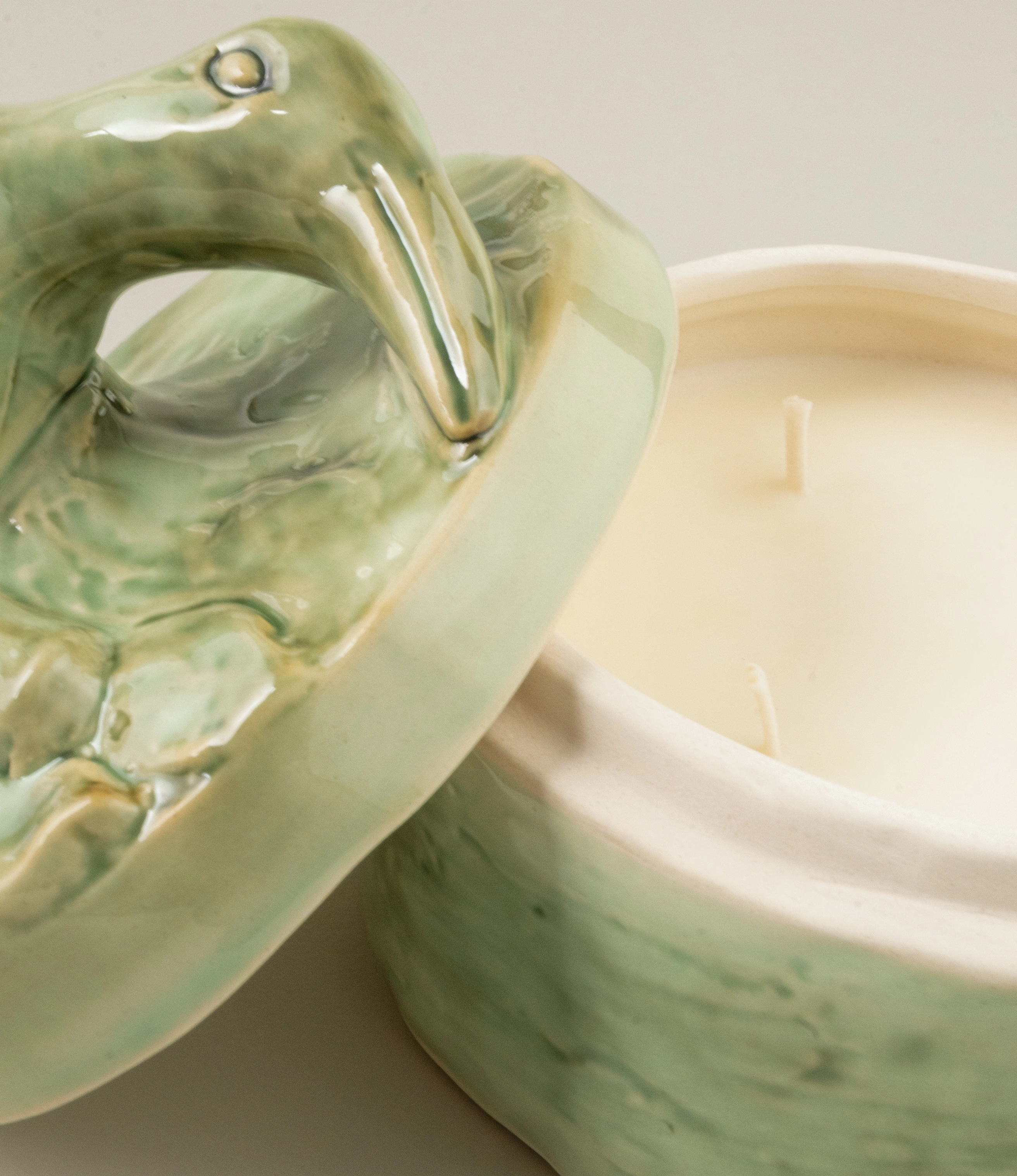 Close-up view of the Serax Green Sonata medium-sized candle showcasing the detailed ceramic lid with an animal-like design and the creamy white wax inside the green container.
