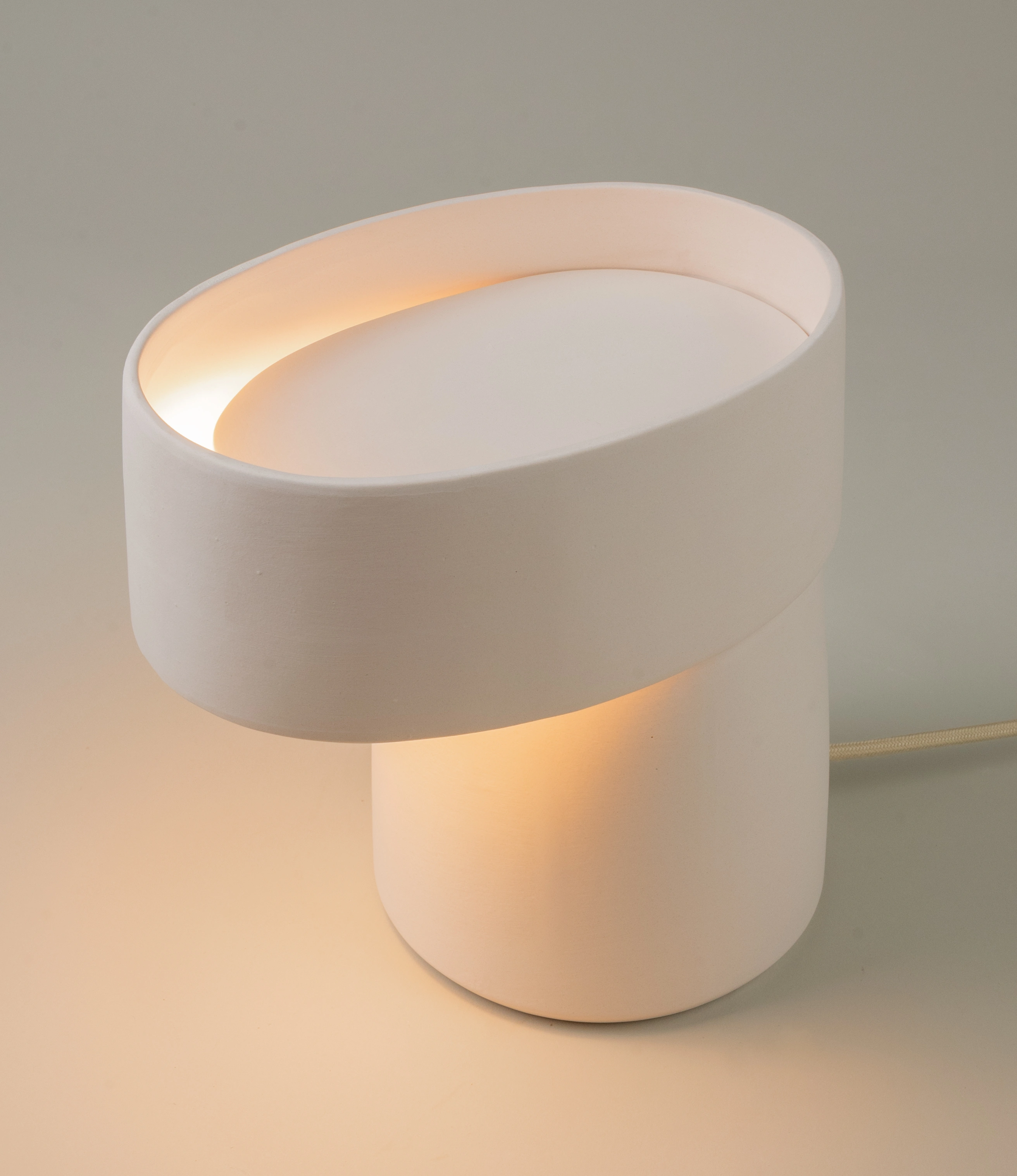A minimalist off-white ceramic table lamp with a sculptural silhouette, softly glowing to create a warm and inviting ambiance. Perfect for elevating modern interiors with a touch of refined simplicity.