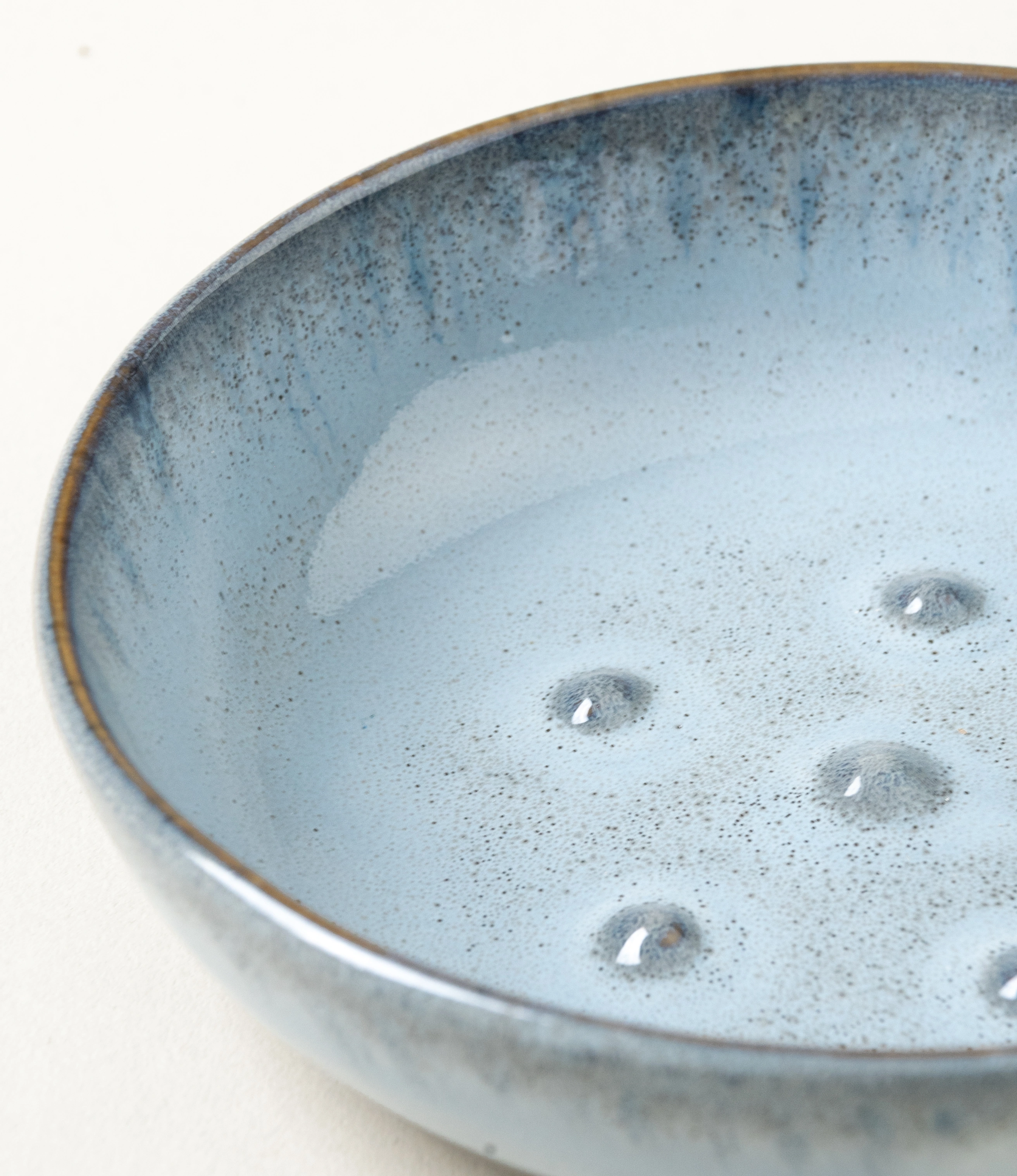 Blue Soap dish from Serax. The round item is made of ceramics and have a blue glazing with a grey unglazed matt area on the bottom. On the edges it has a grey rim. This is a closeup of the product