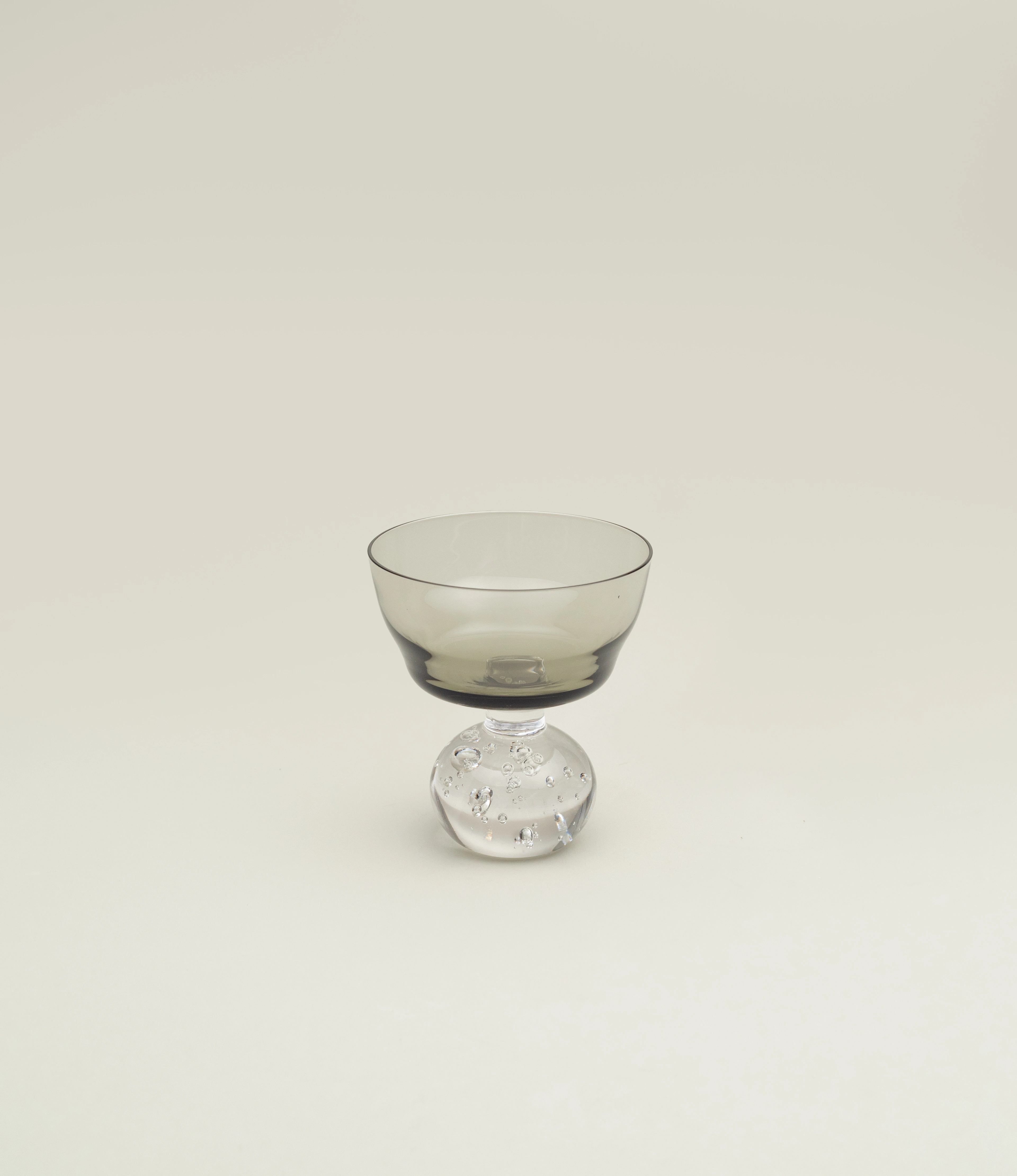 Serax Stem Glass featuring a smoky-tinted bowl and a clear, textured spherical base. A refined and artistic design perfect for serving cocktails or desserts in style.