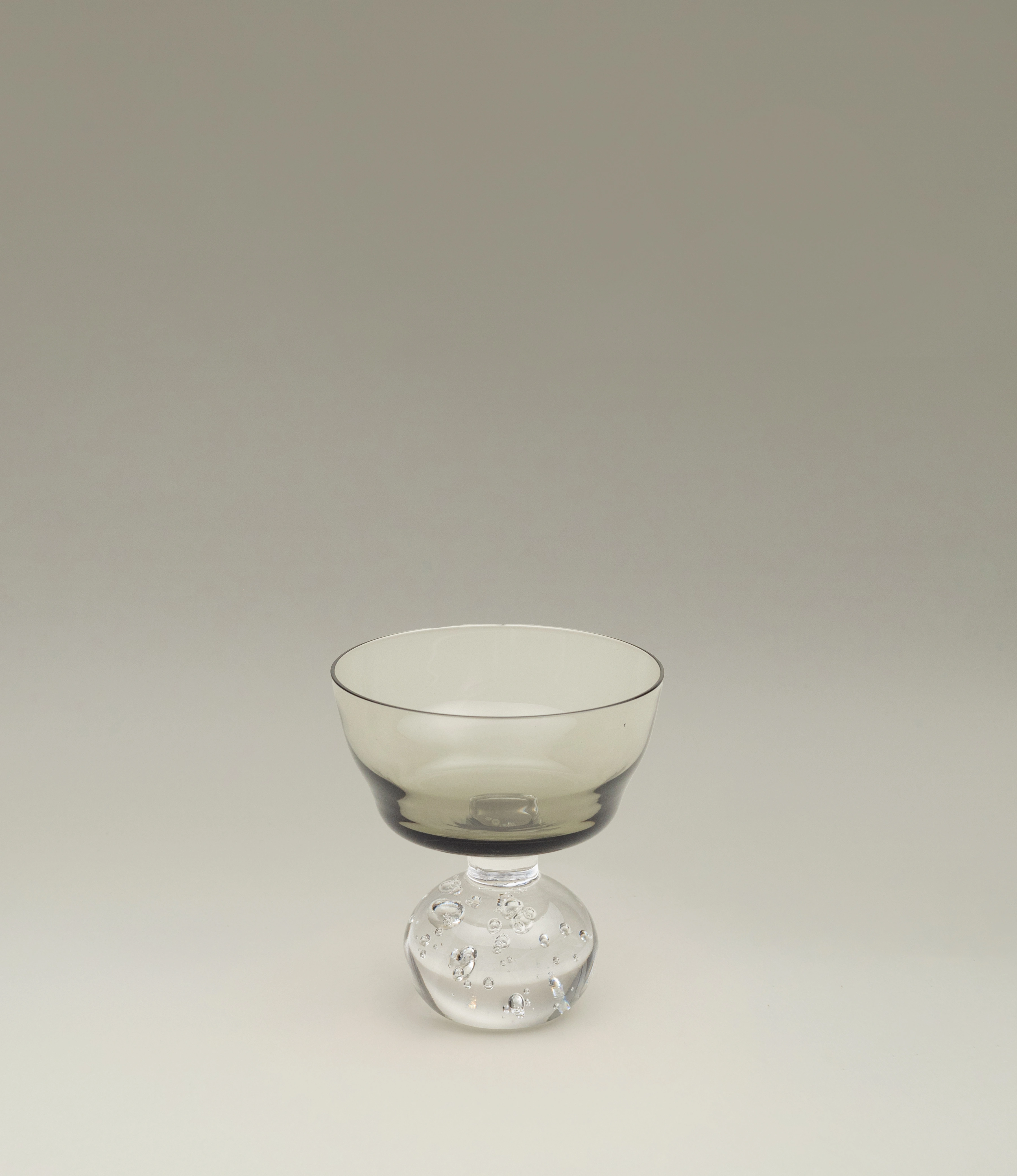 Serax Stem Glass featuring a smoky-tinted bowl and a clear, textured spherical base. A refined and artistic design perfect for serving cocktails or desserts in style.