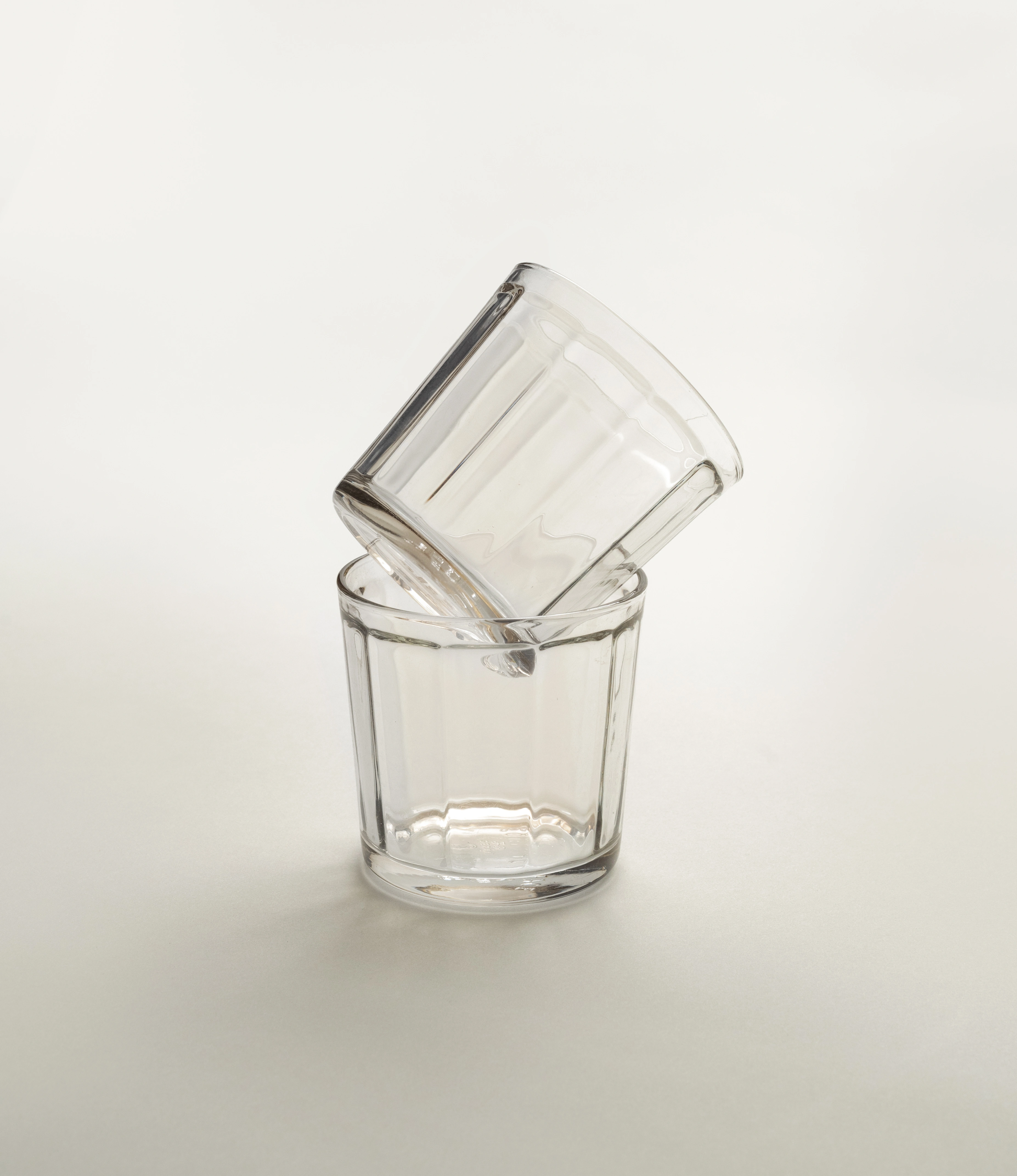 Two clear glass tumblers by Serax, with one glass tilted and resting inside another, displayed on a soft neutral background.