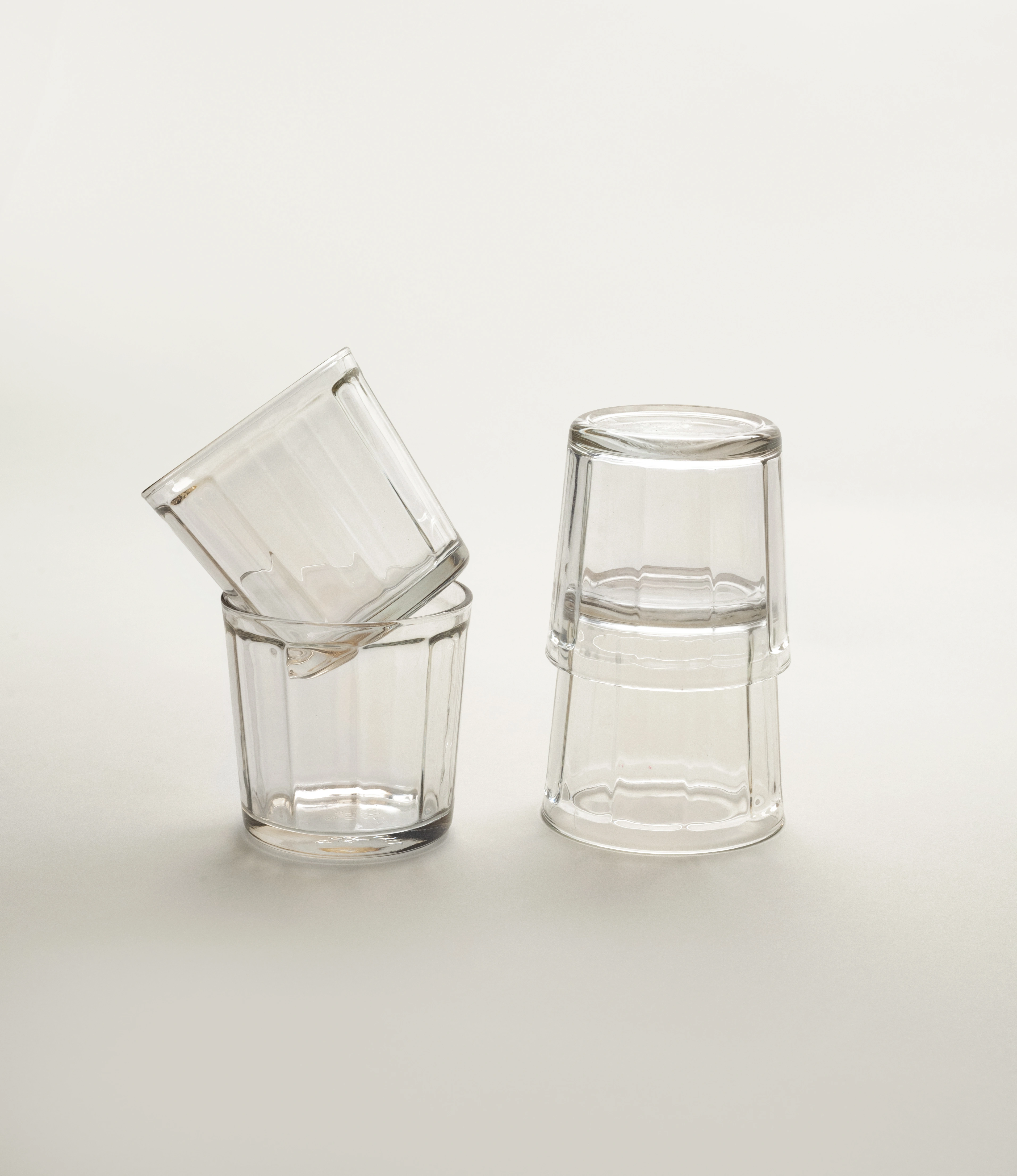 A set of four clear glass tumblers by Serax, with two glasses stacked upside-down and two arranged with one tilted resting inside another, displayed on a soft neutral background.