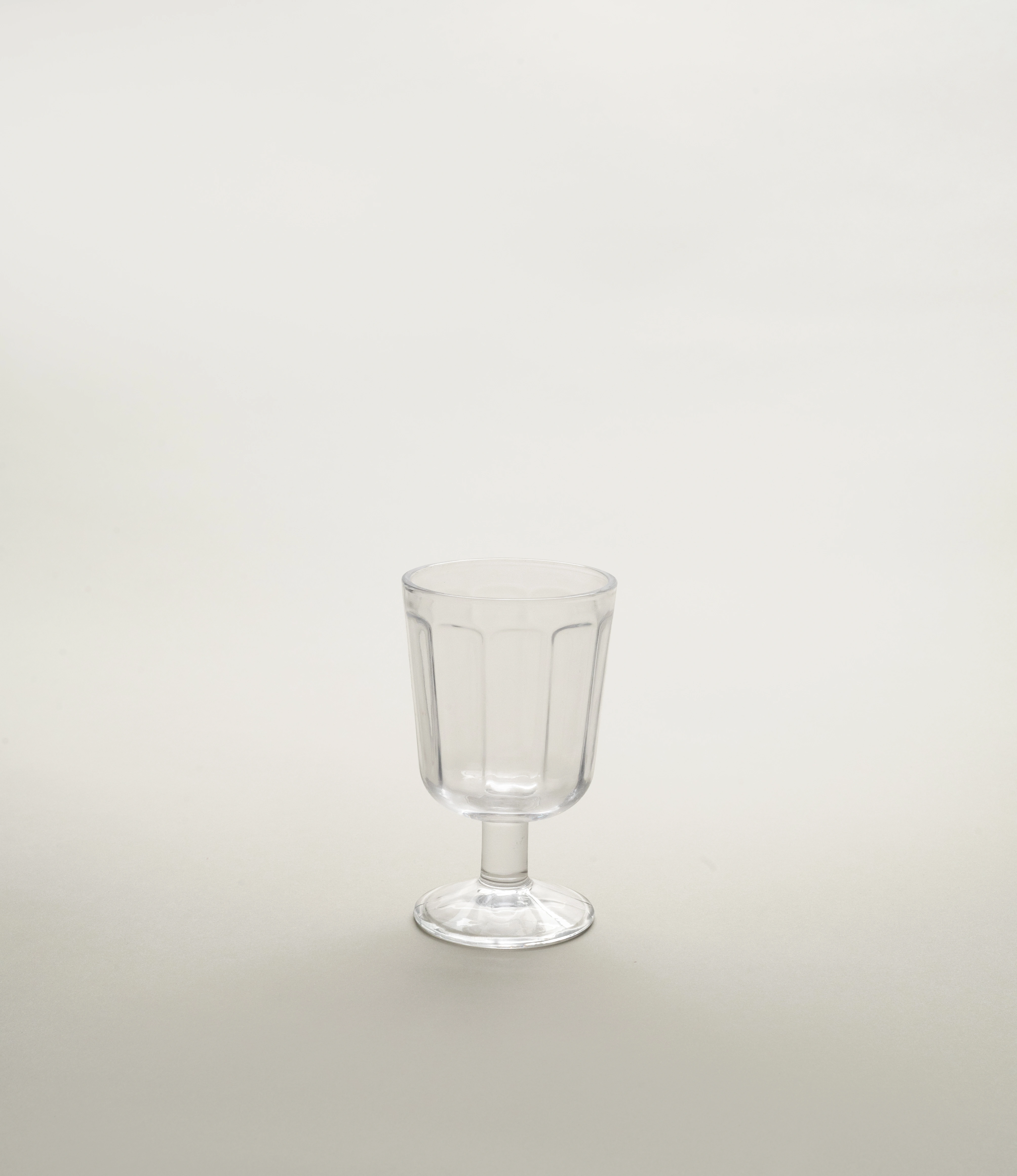 A single clear glass white wine goblet by Serax, showcasing a minimalist fluted design with a short stem, positioned against a light neutral background.