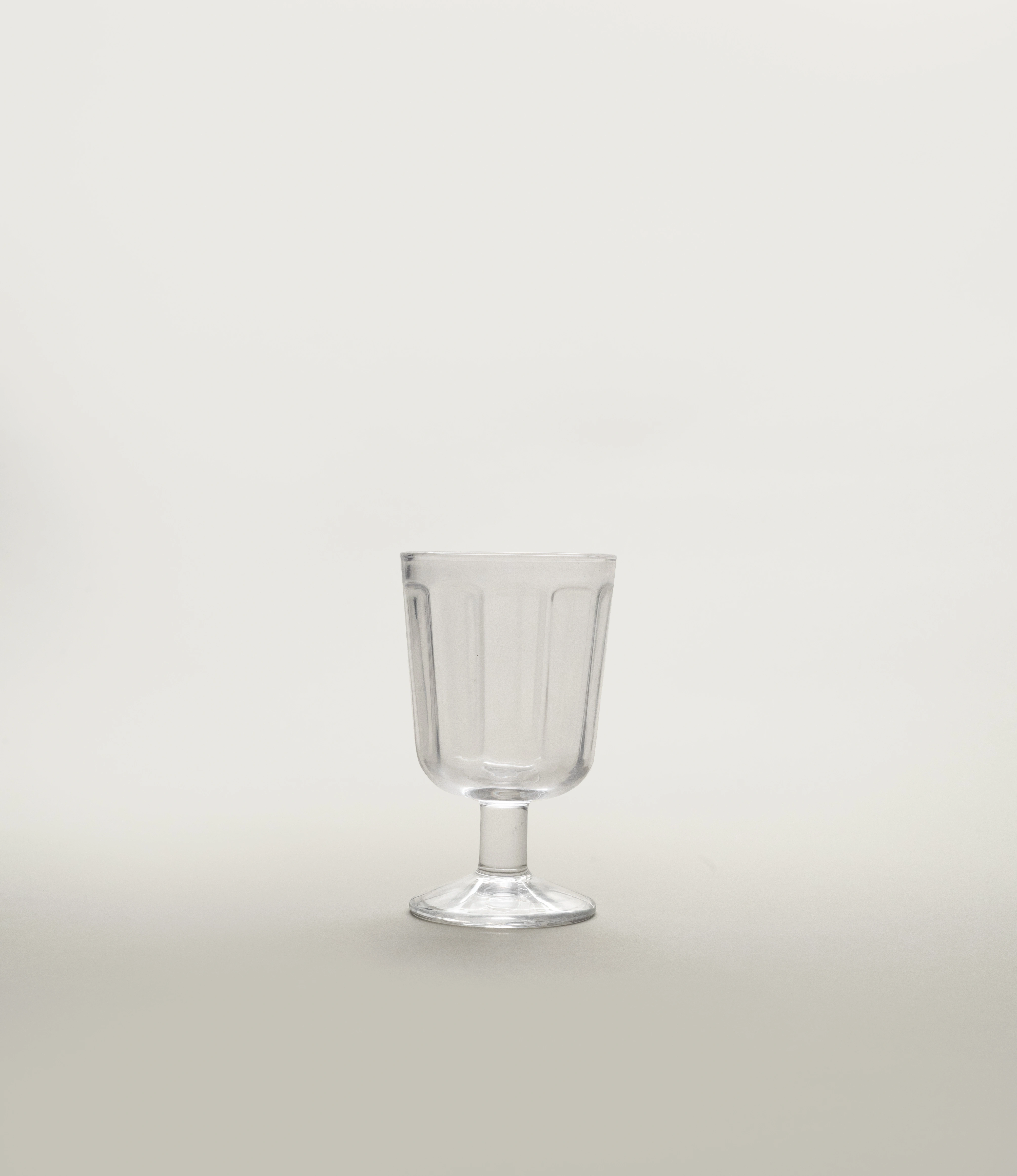A single clear glass white wine goblet by Serax, showcasing a minimalist fluted design with a short stem, positioned against a light neutral background.