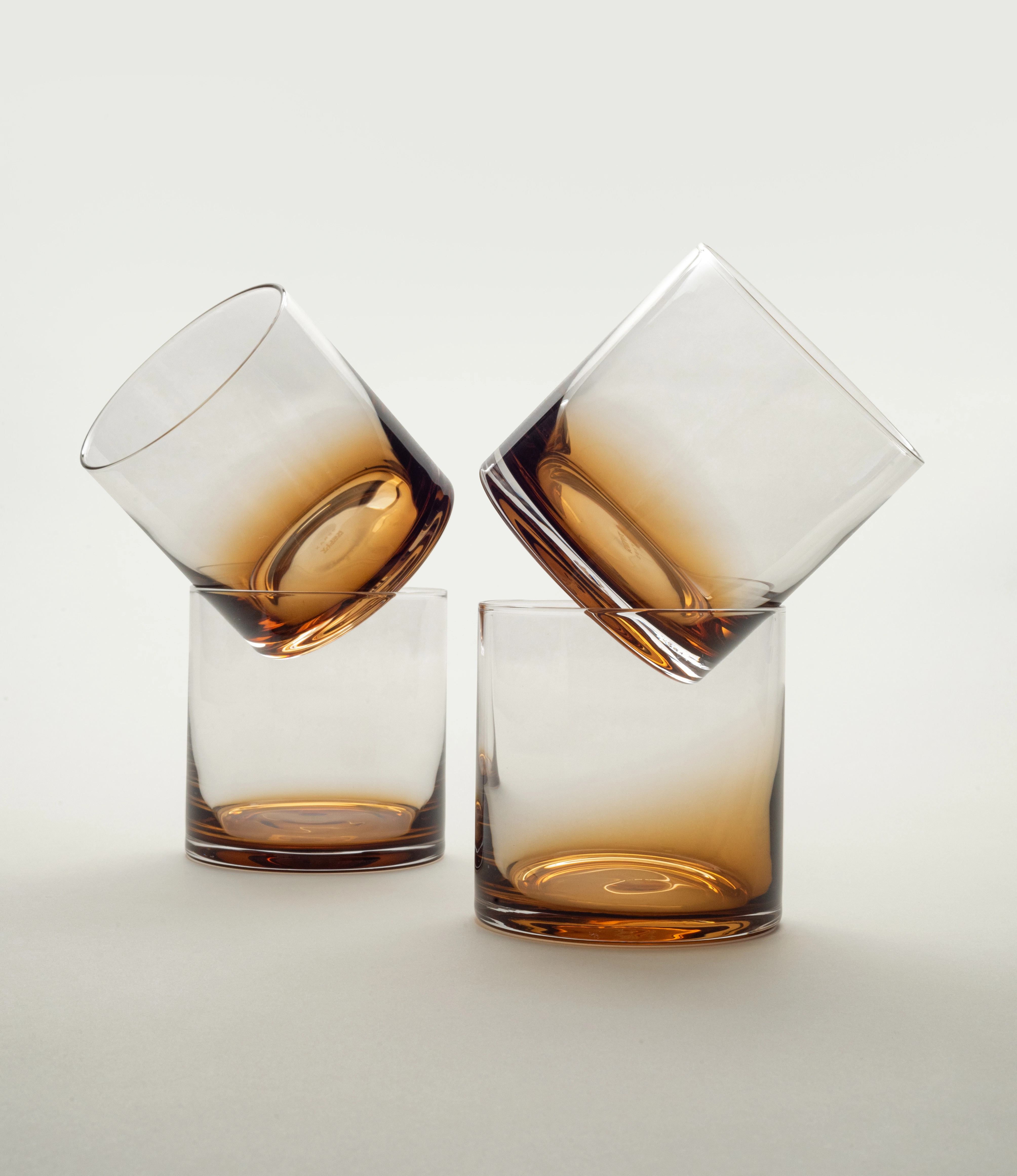Three Serax Zuma whiskey glasses with an amber gradient, two perched at dynamic angles atop the base glasses, highlighting their contemporary aesthetic on a clean, minimal background.