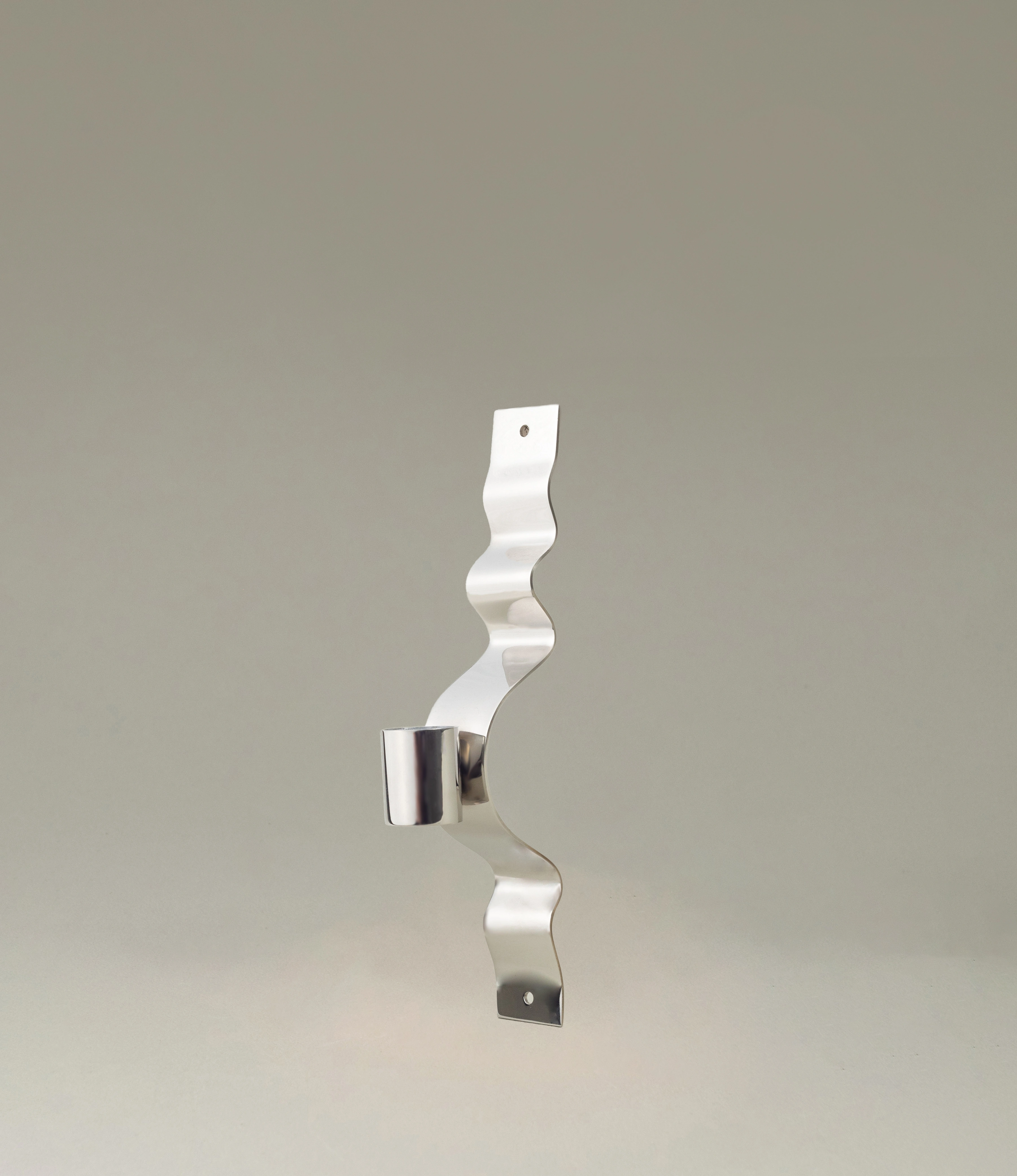 Wave Wall Candle Holder from Stences is ment to be hanged on your wall. The polished stainless steel item is attached to your wall with the ribbon-like wavy chrome part behind the part that holds your taper candle.