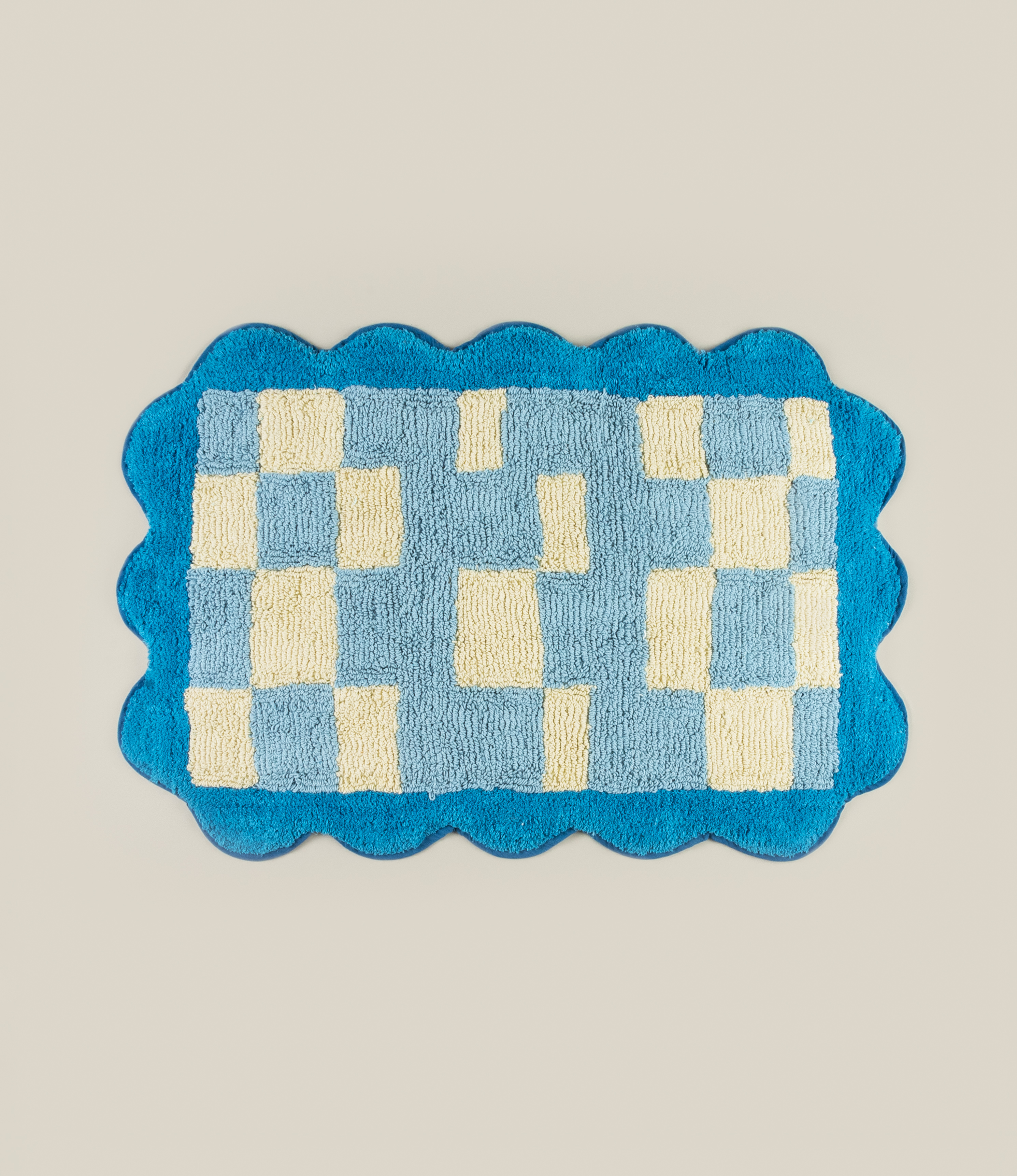 Tarta Gelatina's Burbuja Bathmat, a 100% cotton bathmat with a blue and cream checkered design and wavy border.