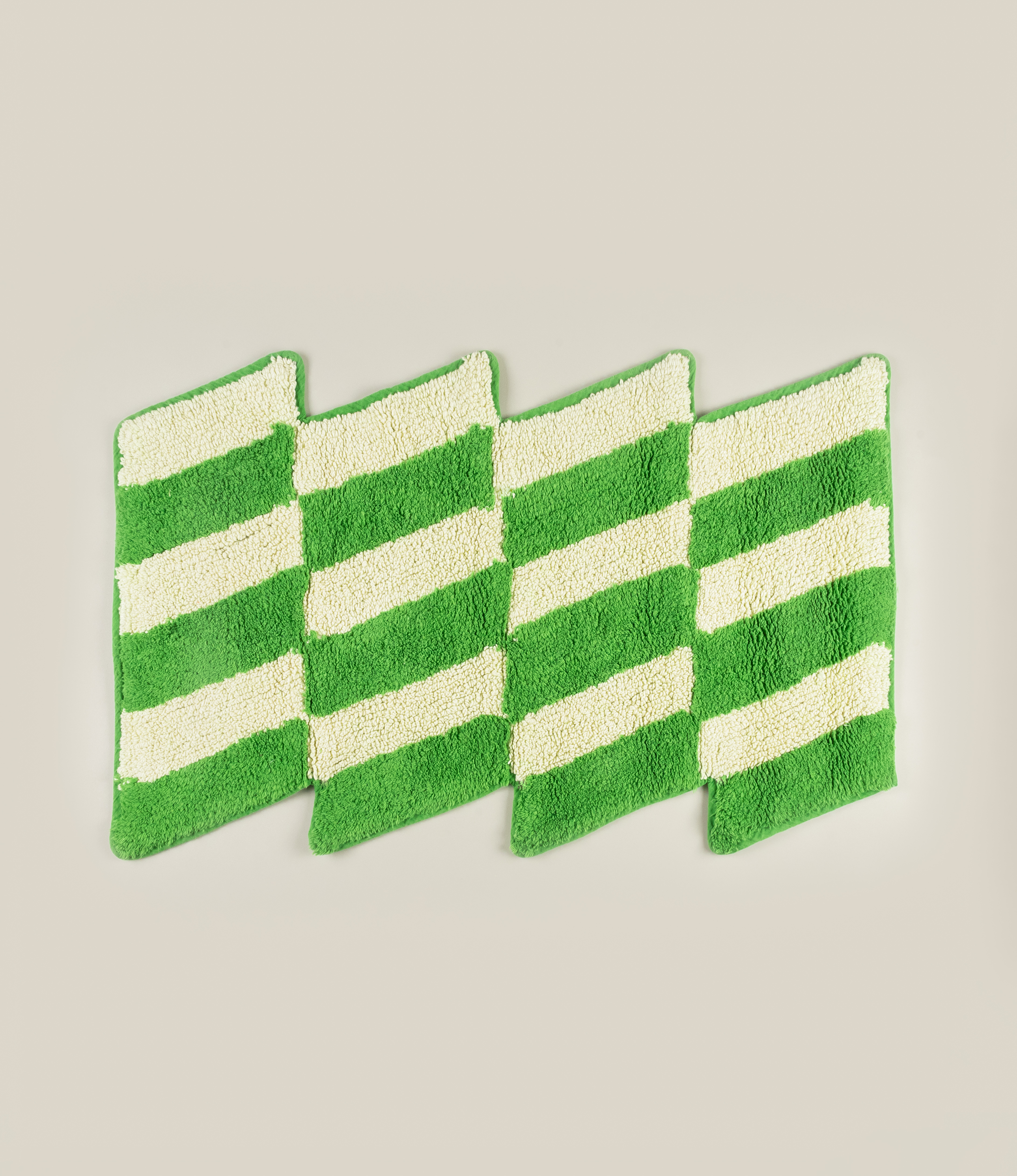 Casette Bathmat by Tarta Gelatina, featuring a bold green and cream diagonal stripe pattern with a zigzag silhouette, made from 100% cotton