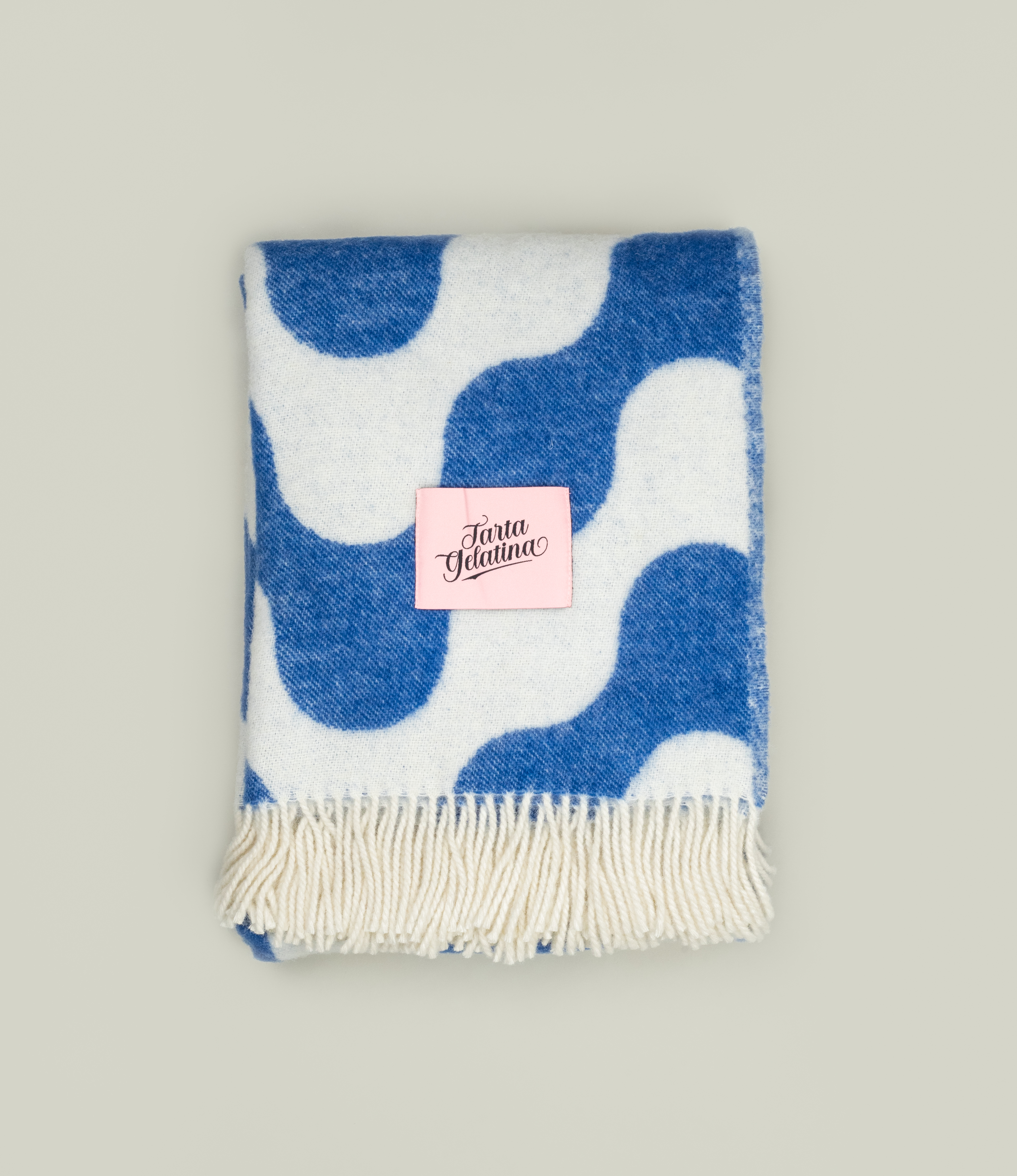 Medusa Blanket folded with Tarta Gelatina label – A neatly folded wool blanket with a soft pink Tarta Gelatina label, featuring its signature wave-like design.