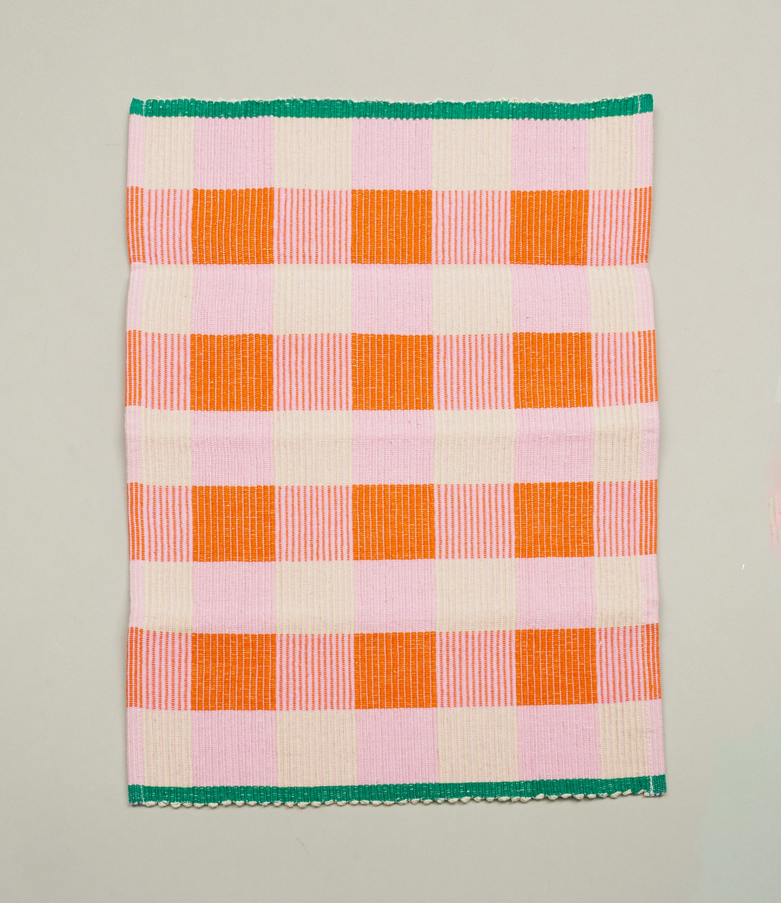 Pink and orange variant of Tarta Gelatina's Merienda Placemats. The item has a checkered pattern and it has a green edge on the shorter sides.