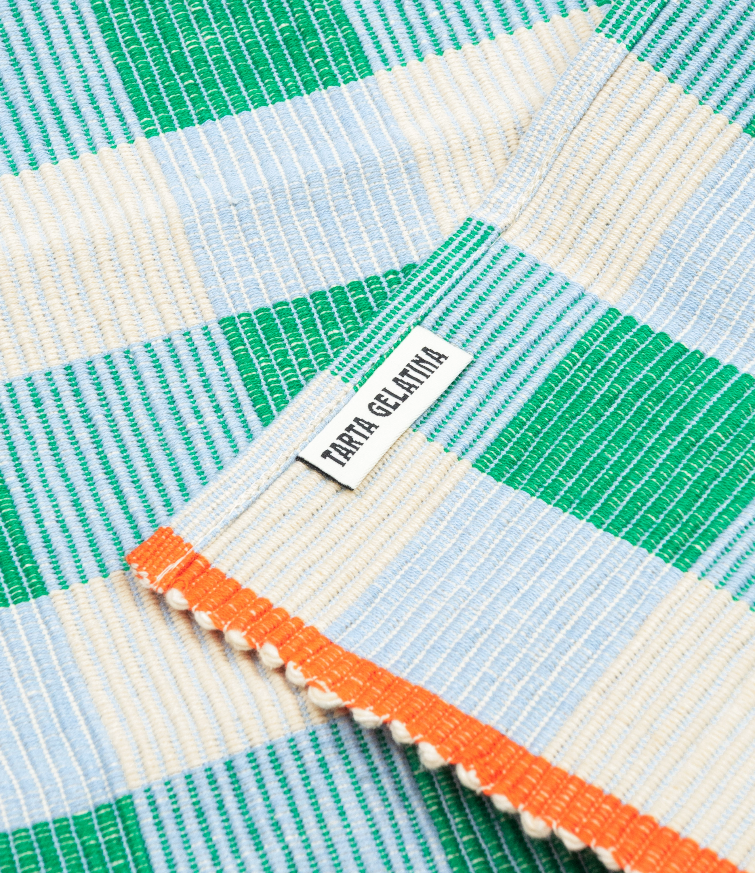A close-up picture of a Merienda Placemat from Tarta Gelatina. This particular placemat has a light blue and green checkered pattern with an orange edge on the sides of the placemat.