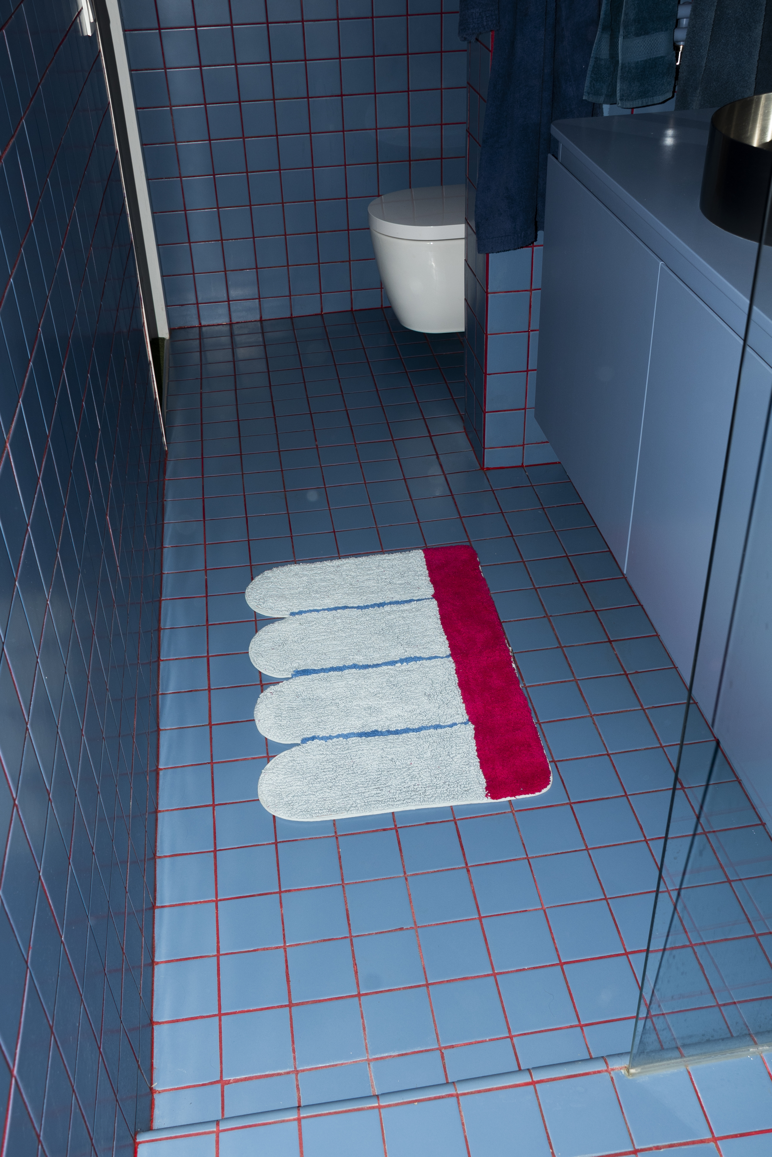 Overhead shot of Tarta Gelatina's Poolside Bathmat in a modern bathroom setting, adding a pop of color against the deep blue tiles.