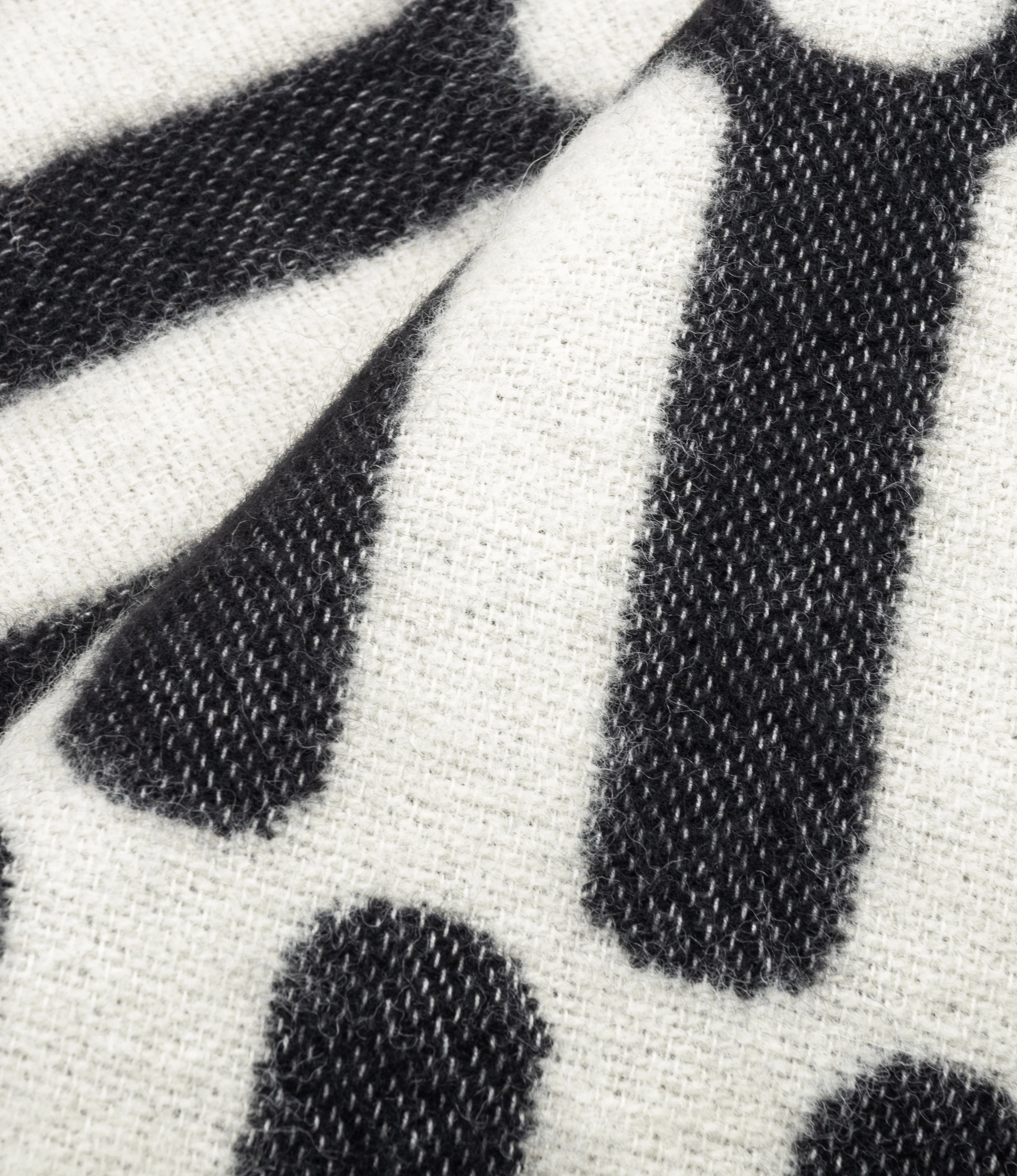 A detail picture of the Throw Blanket From Tarta Gelatina in a black and white color. The pattern is similar to what you would see on op-art pictures.