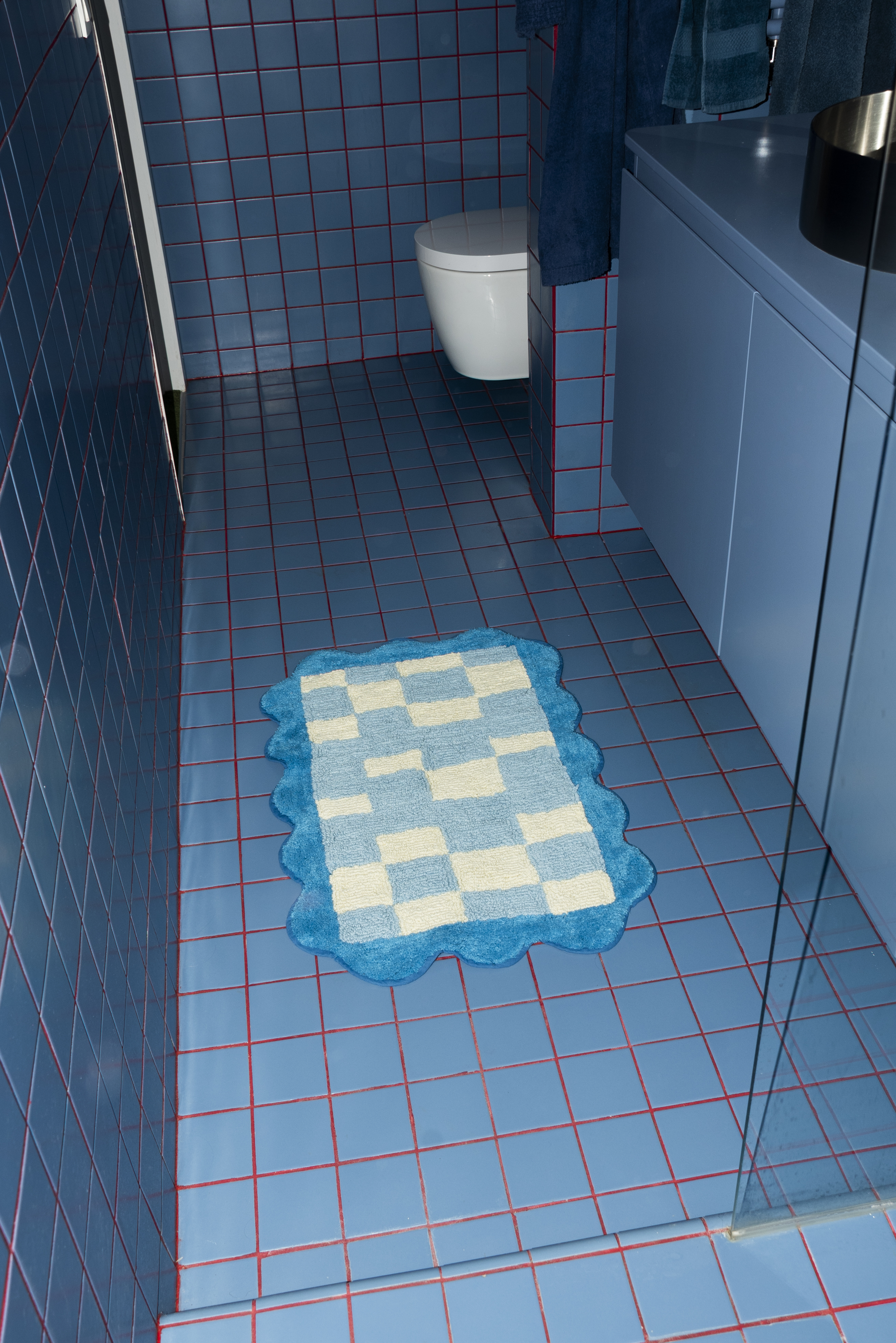 Close-up of the Tarta Gelatina's Burbuja Bathmat placed on blue floor tiles, showcasing its soft texture and geometric checkerboard design.