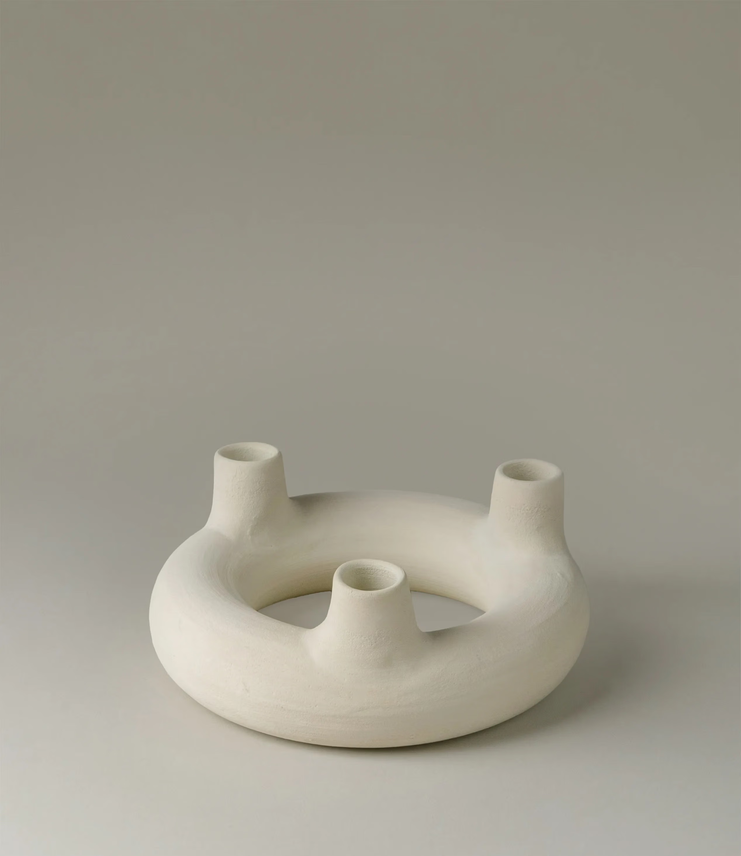 Chandelier Rotulis is a candle holder designed by Alfareria La Nava. The item can hold three candles arranged on a rounded shape. It has a matte raw white color.