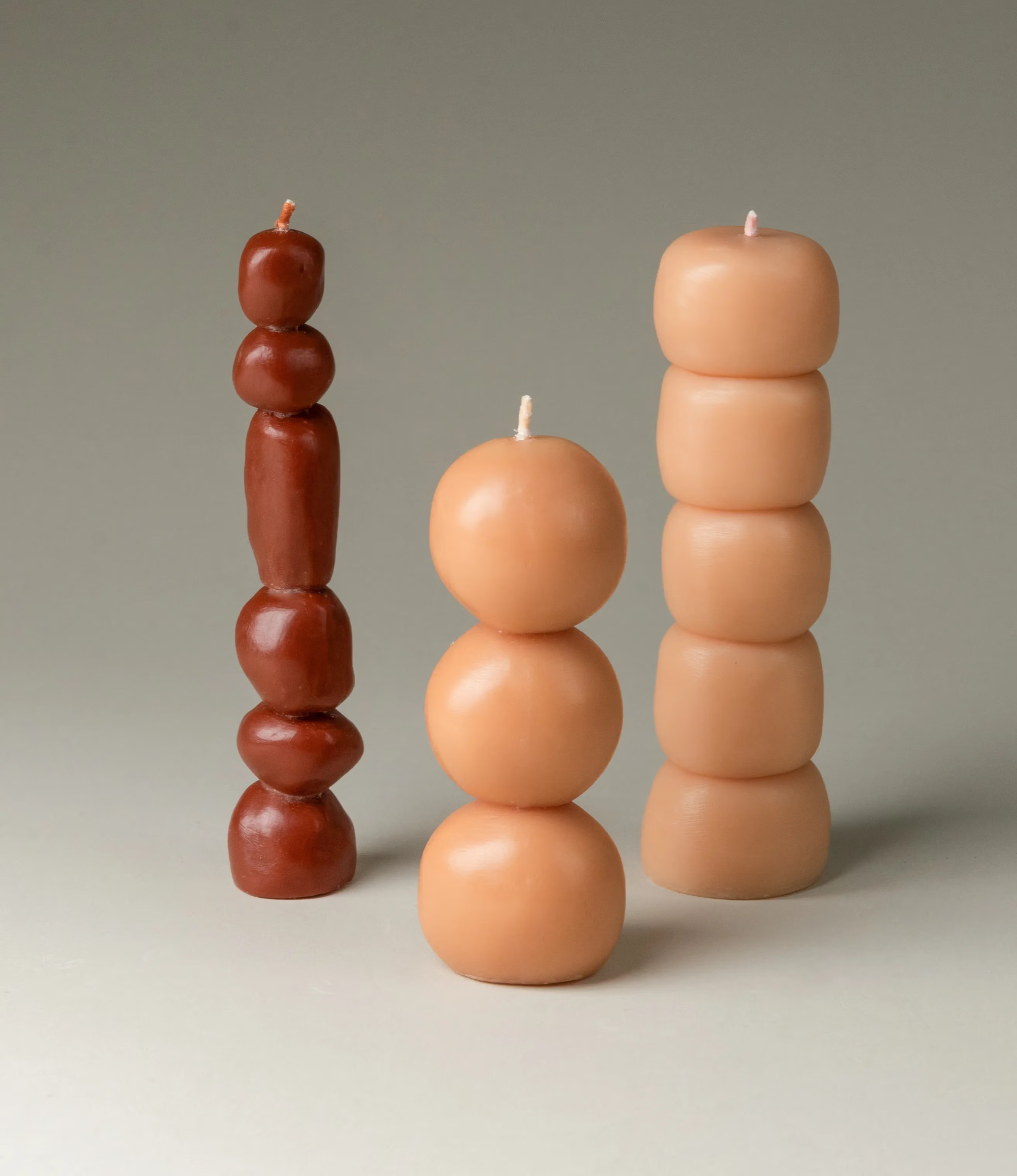 A packshot of the Piu set which contains three candles from Ann Vincent. One candle comes in a dark burgundy color the other two are beige. The candles look like little balls or stones stacked on top of each other.